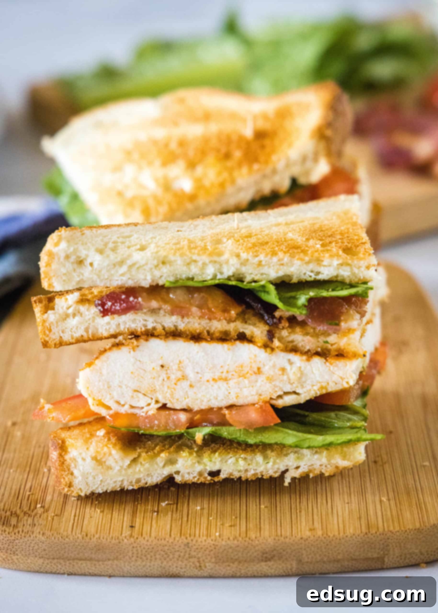 Close up of one half of a perfectly assembled chicken club sandwich, showcasing its layers of ingredients, resting on a rustic wooden cutting board.