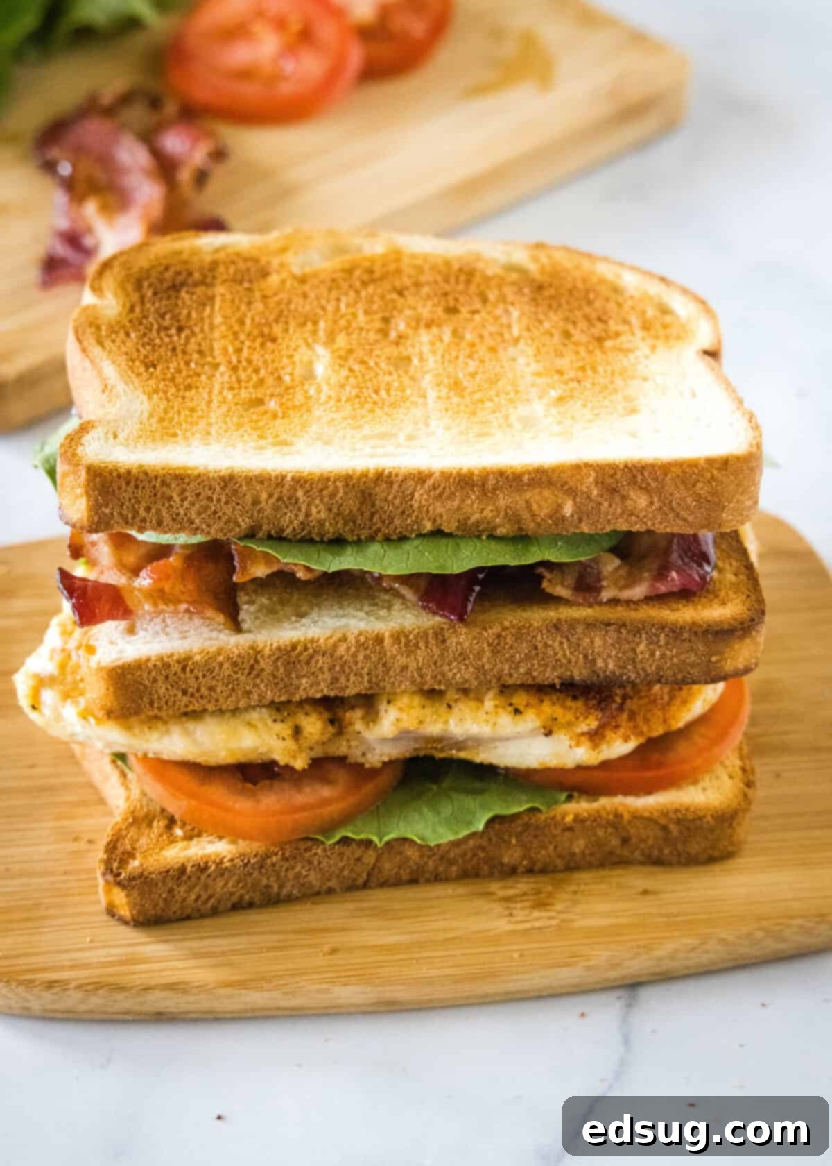 A fully assembled chicken club sandwich, showing all three layers neatly stacked and ready to be sliced, sitting on a wooden cutting board.