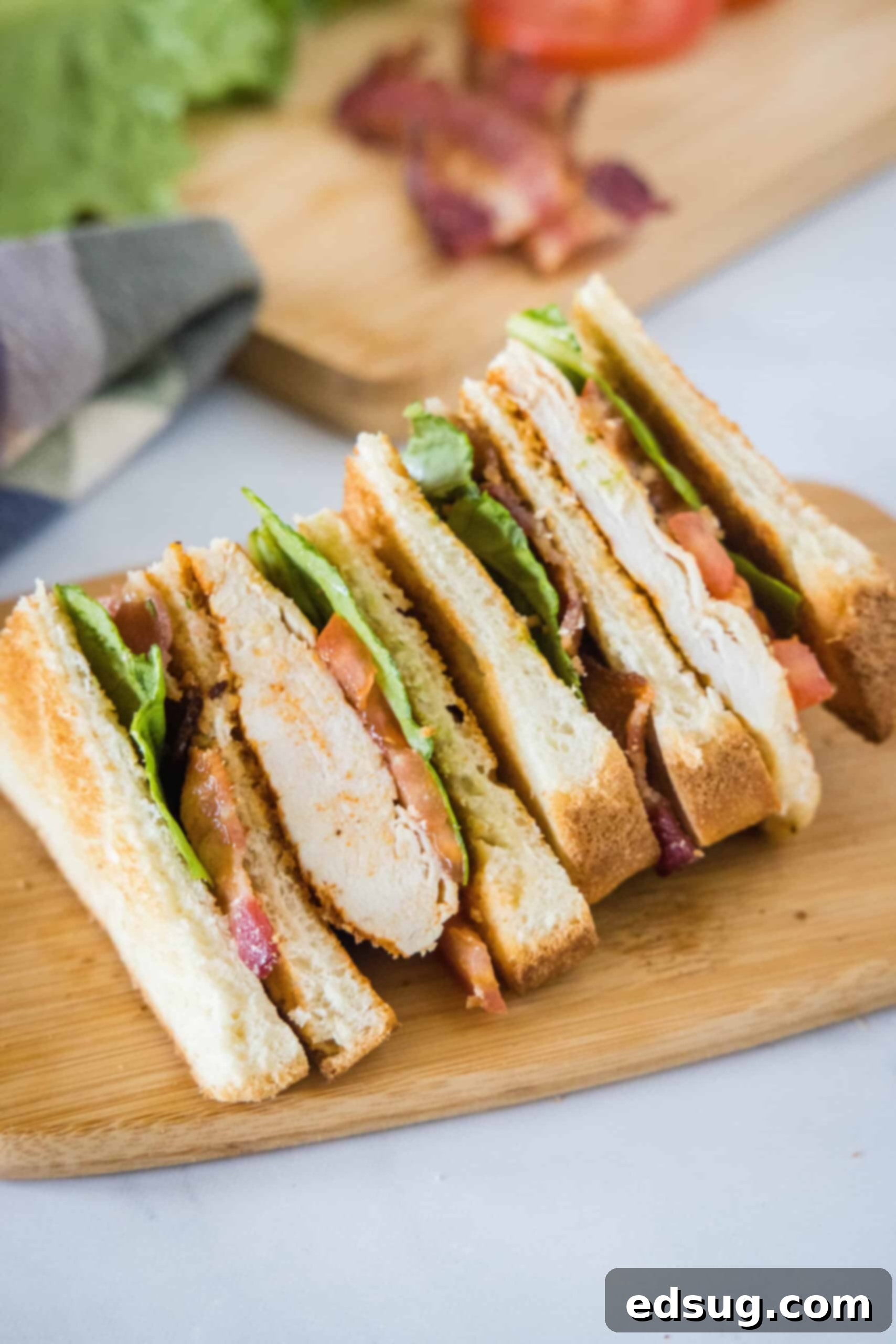 A beautifully presented chicken club sandwich, neatly cut into two halves, revealing its delectable layers, served on a wooden cutting board.