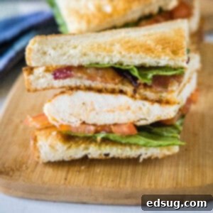Close up of one half of a chicken club sandwich on a wooden cutting board.