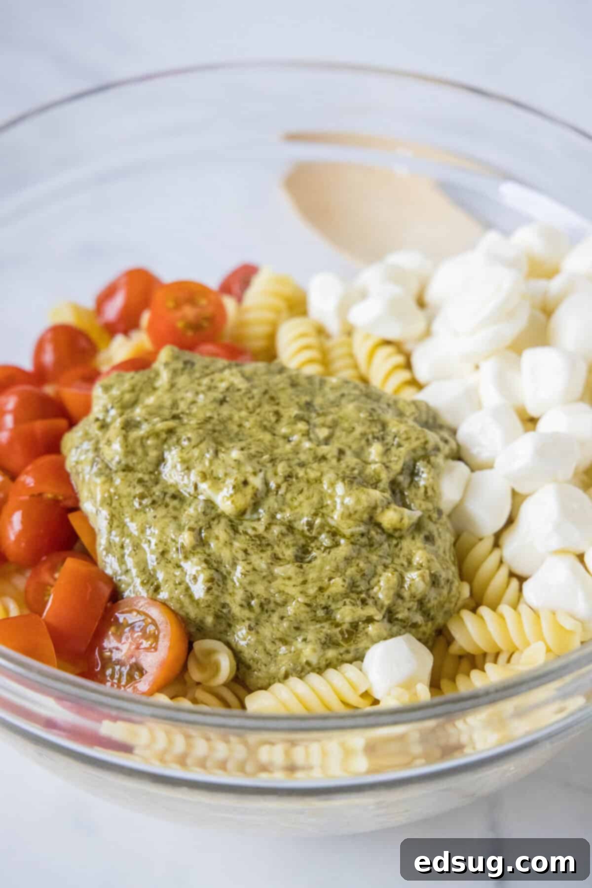 adding pesto dressing to pasta, tomatoes and mozzarella