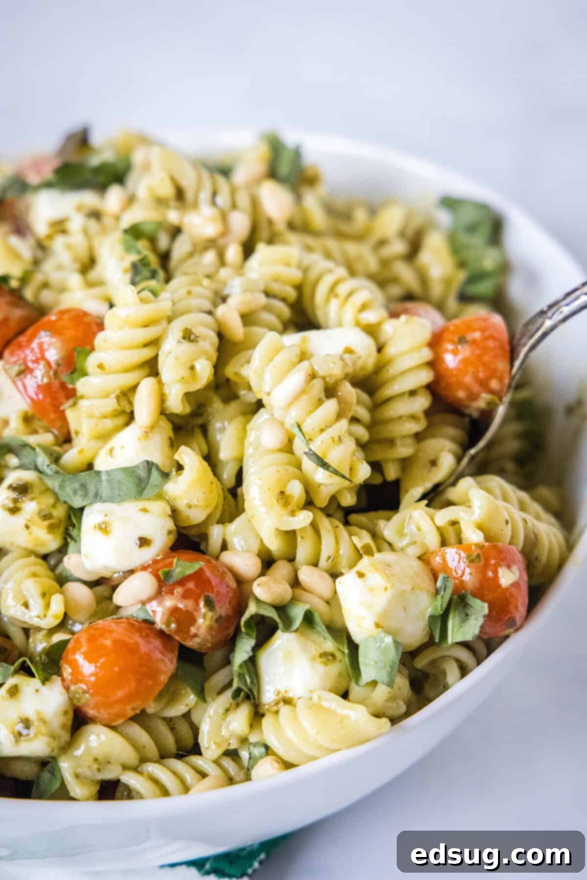 a spoon scooping out pesto pasta salad from a serving bowl