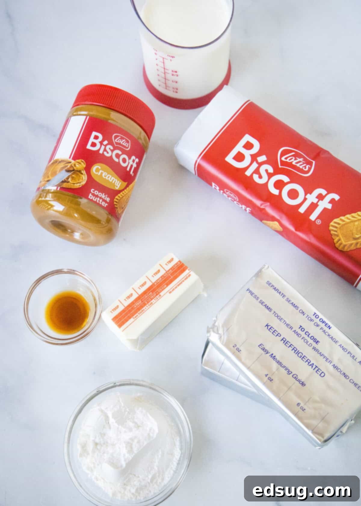 A collection of ingredients laid out, including Biscoff cookies, cream cheese, heavy cream, butter, and Biscoff spread, ready for making cheesecake.