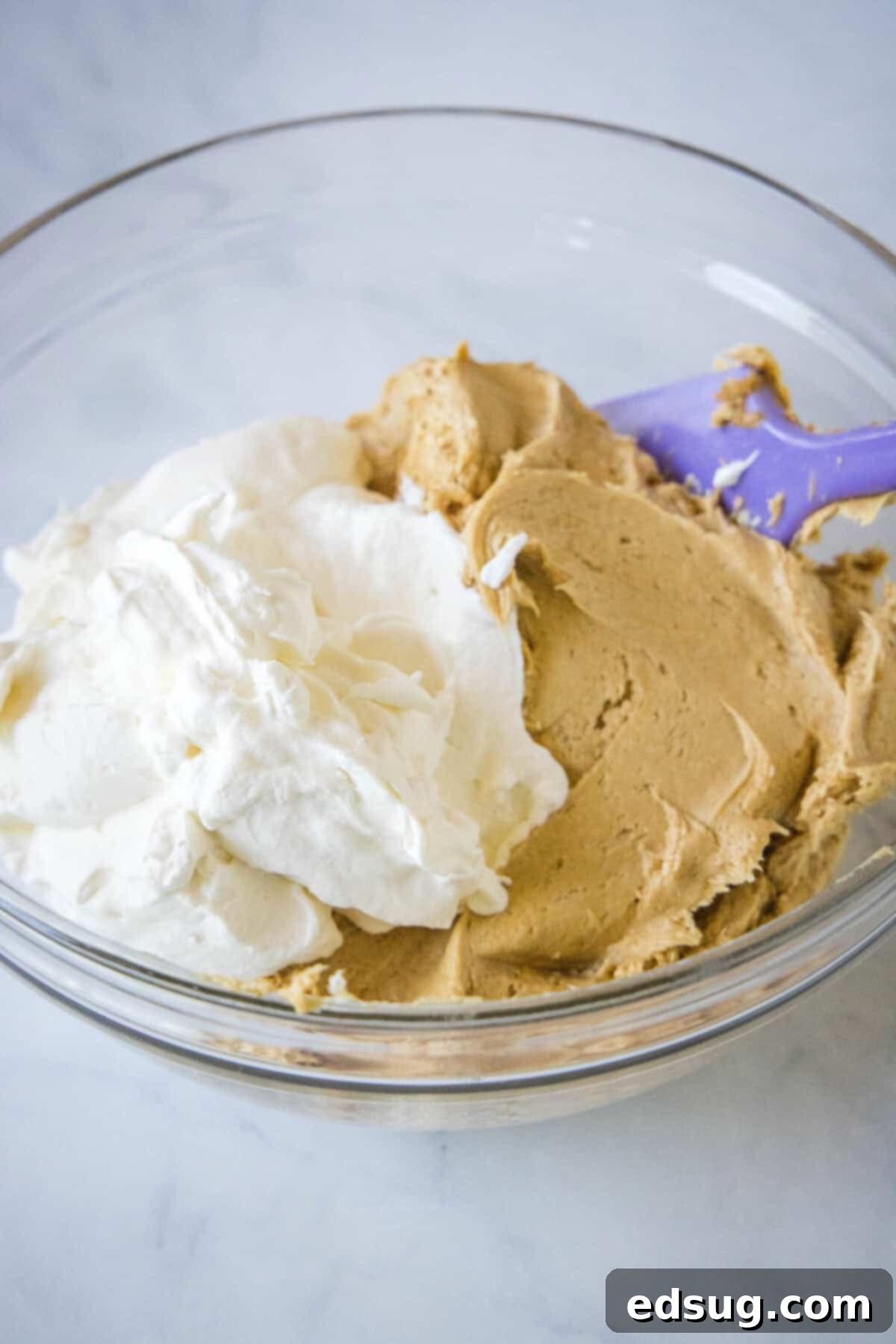 A mixing bowl holding a creamy blend of cream cheese and Biscoff spread, alongside a bowl of freshly whipped cream.