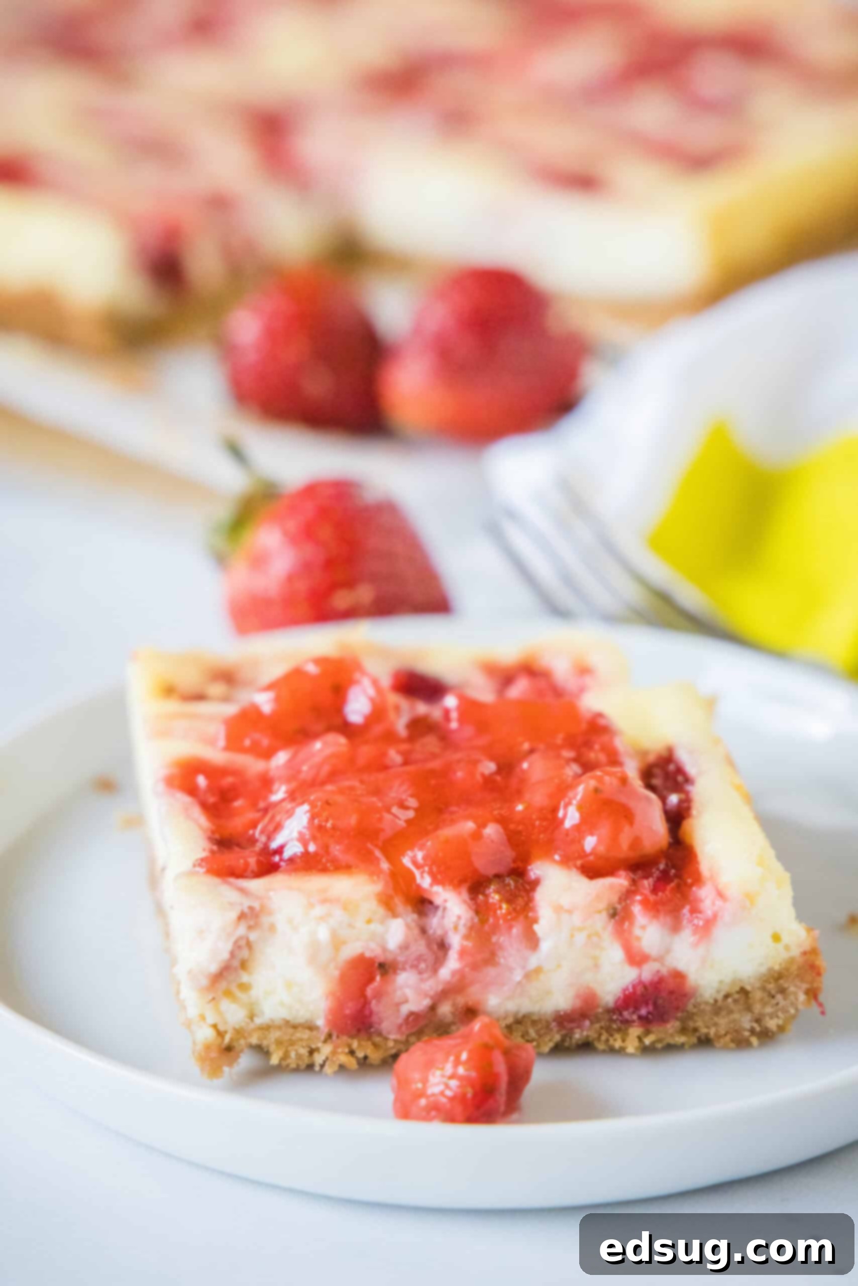 These strawberry cheesecake bars have a tangy cream cheese filling swirled with gooey strawberries, baked on top of a graham cracker crust. A strawberry cheesecake bar topped with strawberry compote on a plate.