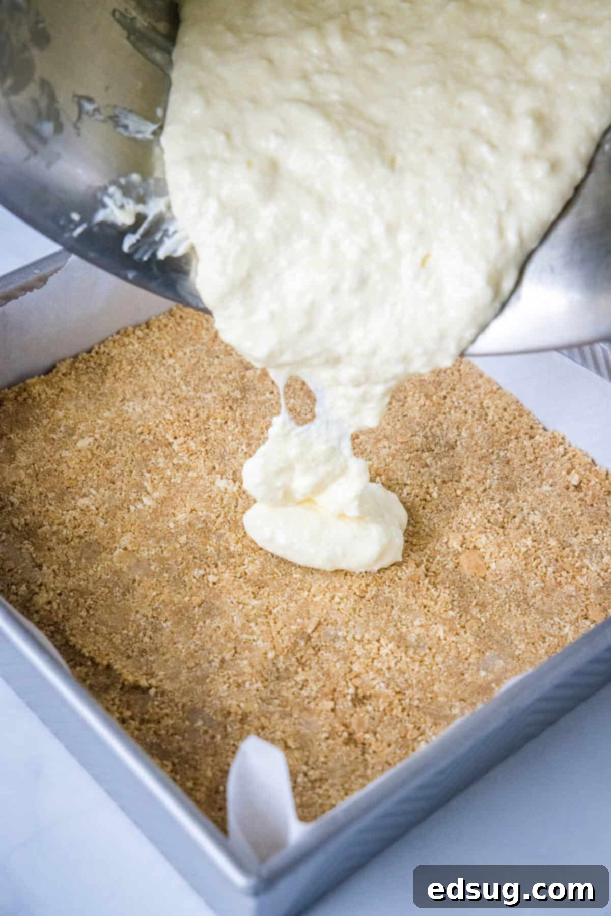 These strawberry cheesecake bars have a tangy cream cheese filling swirled with gooey strawberries, baked on top of a graham cracker crust. Cheesecake filling being poured over a prepared graham cracker crust in a baking dish.