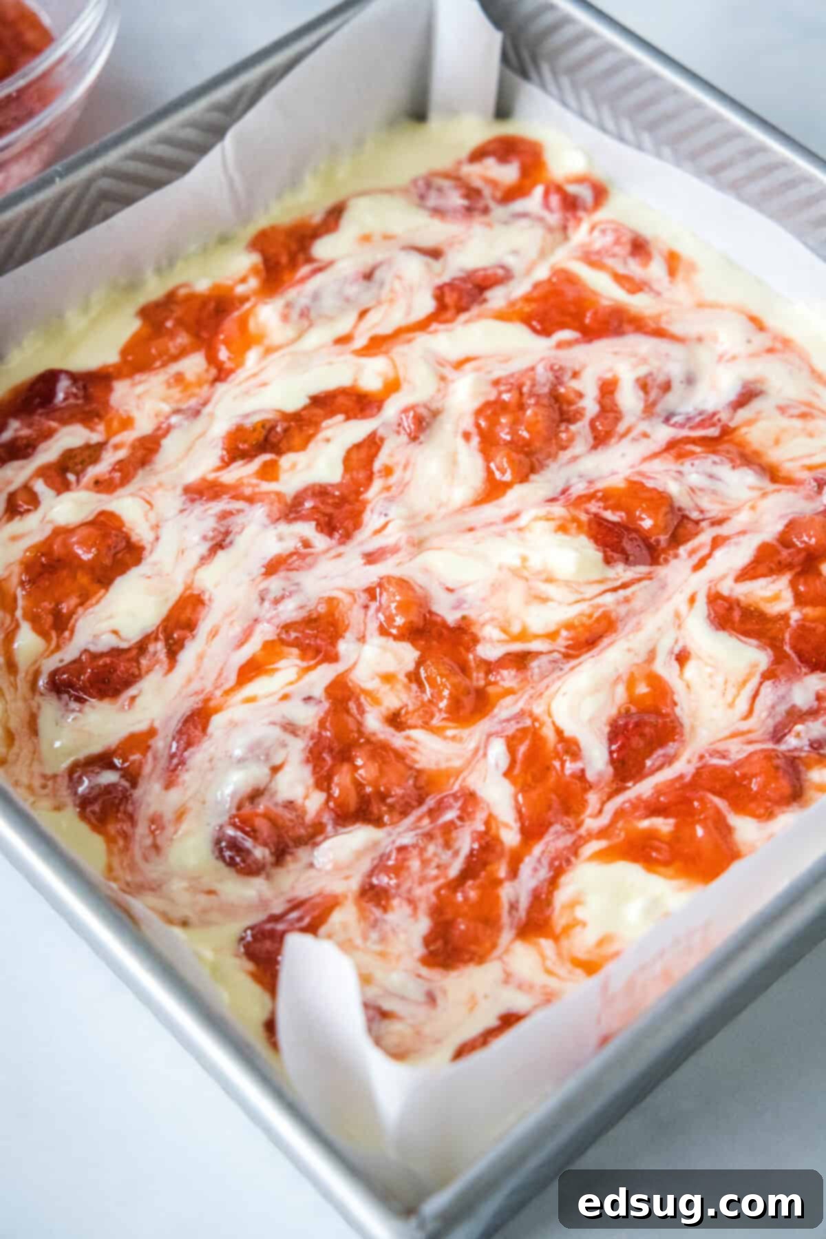 These strawberry cheesecake bars have a tangy cream cheese filling swirled with gooey strawberries, baked on top of a graham cracker crust. Unbaked strawberry cheesecake bars assembled in a baking dish.