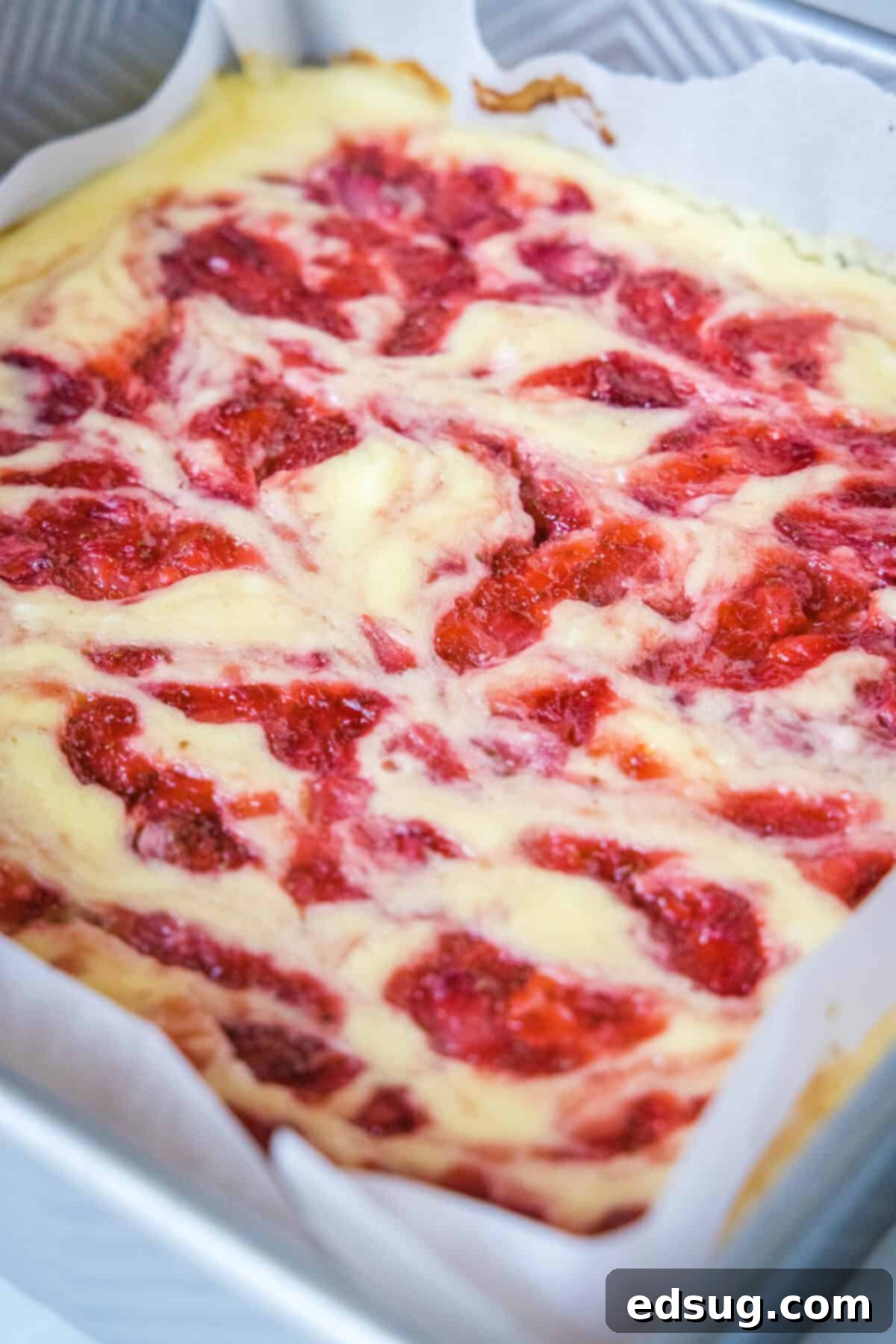 These strawberry cheesecake bars have a tangy cream cheese filling swirled with gooey strawberries, baked on top of a graham cracker crust. Baked strawberry cheesecake bars in a baking dish.