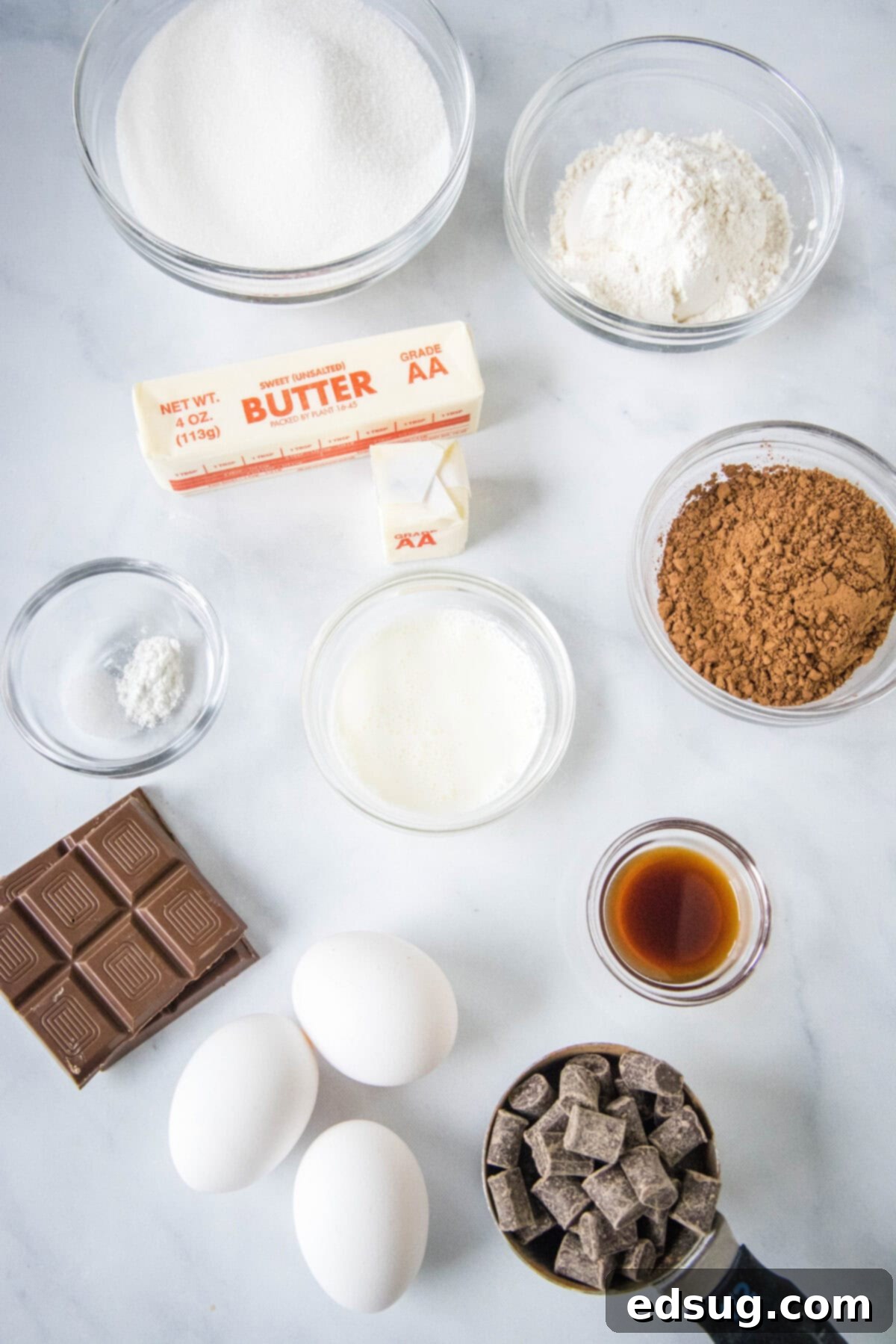 Decadent Chocolate Chunk Brownies 3 Various ingredients for chocolate chunk brownies laid out on a surface, including butter, chocolate, sugar, eggs, heavy cream, vanilla, flour, cocoa powder, salt, baking powder, and chocolate chunks.