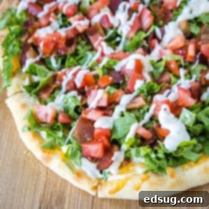 Close up of a BLT pizza topped with a drizzle of aioli on a wooden cutting board.
