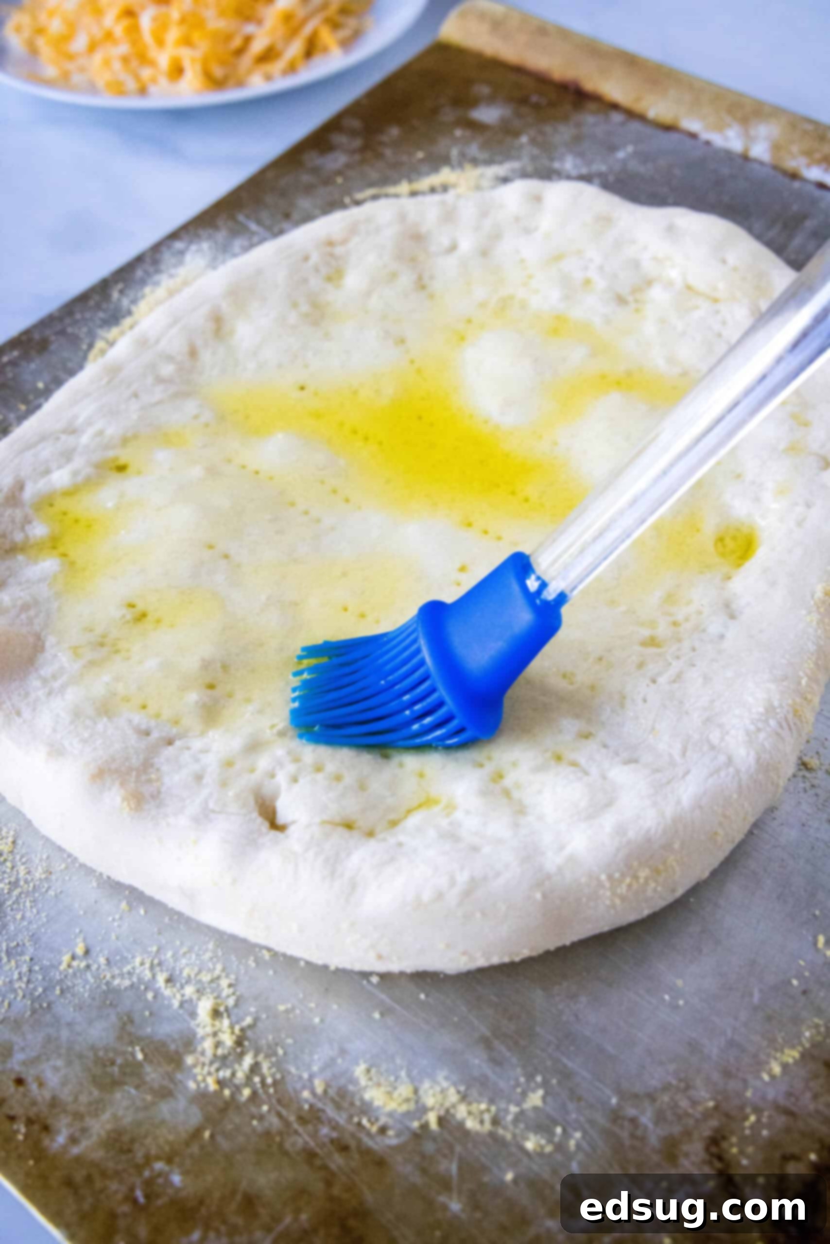 A rubber basting brush coating the top of a par-baked crust with olive oil.
