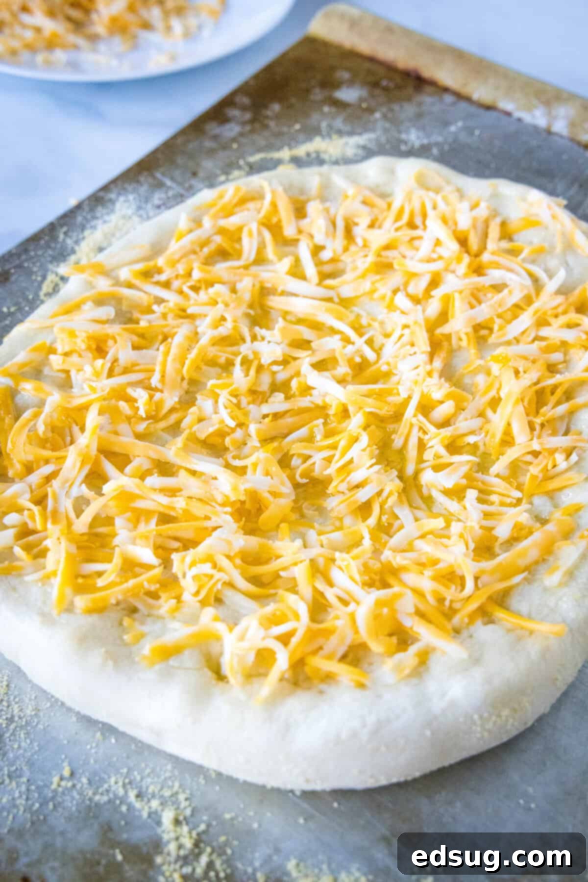 A par-baking pizza crust topped with shredded cheese on a baking sheet.