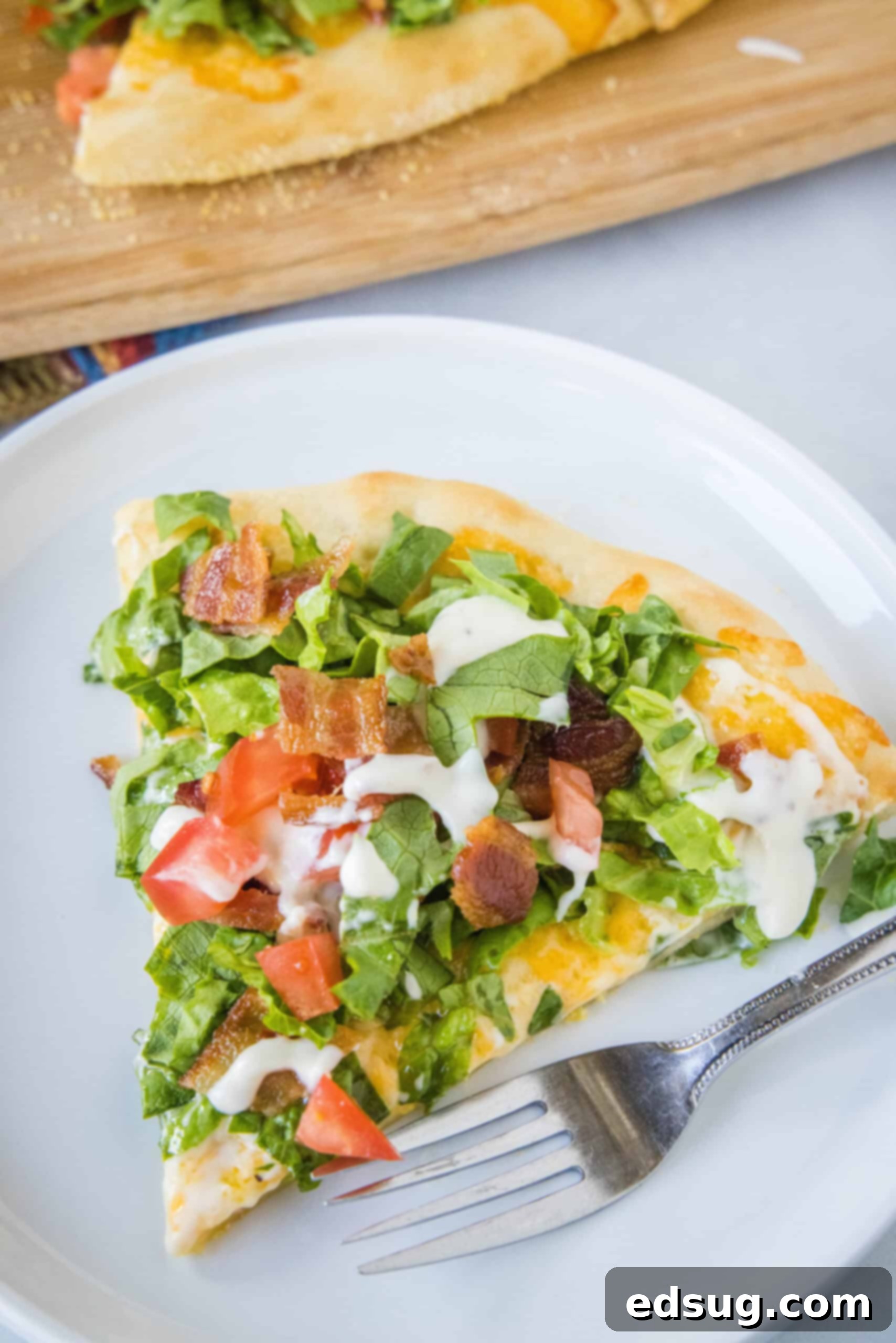 A slice of BLT pizza on a white plate next to a fork.