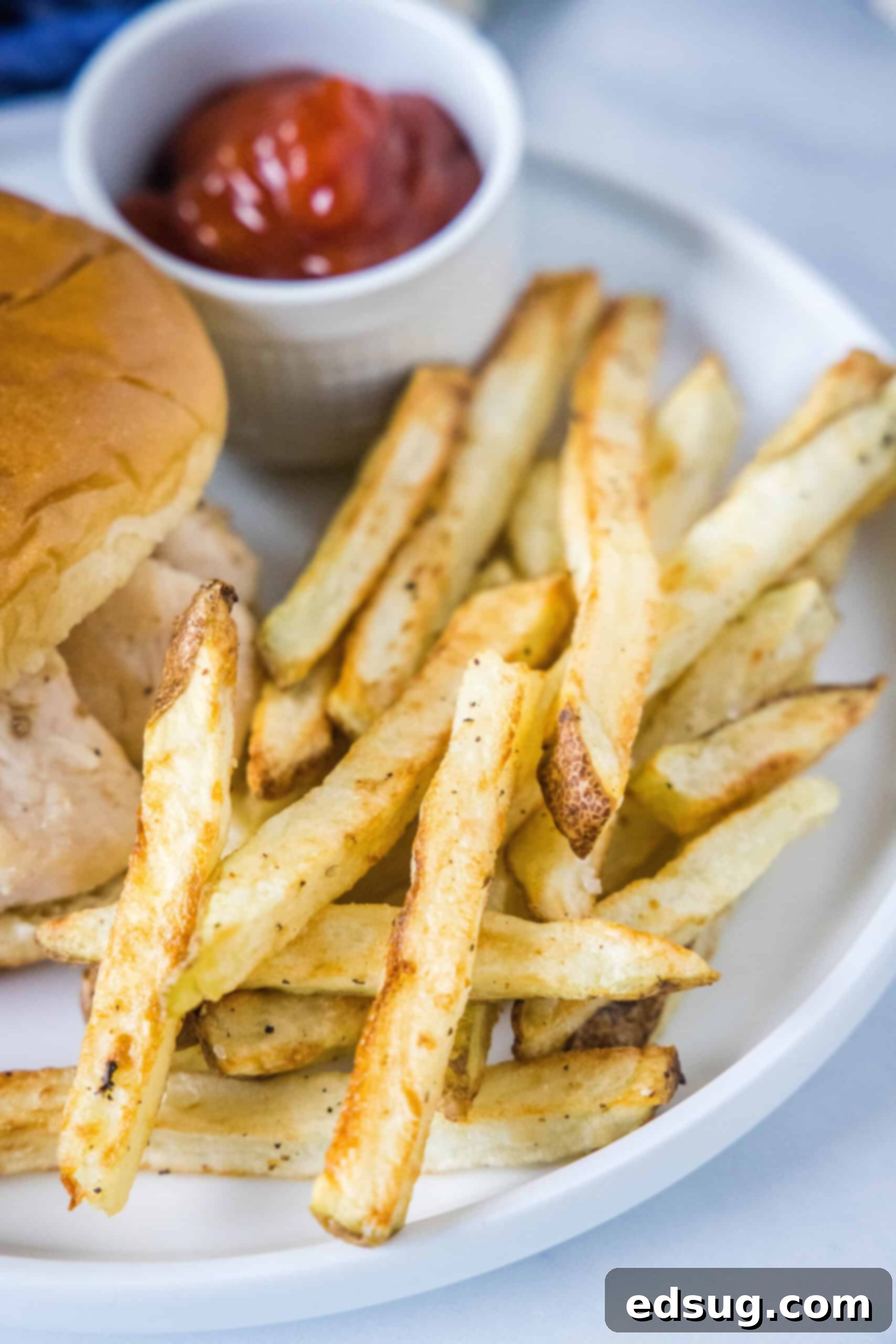 Homemade air fryer French fries are just as crispy as regular fries! Make them in a fraction of the time, with any seasonings you’d like. Homemade air fryer French fries next to a burger and a small ramekin filled with ketchup on a plate.