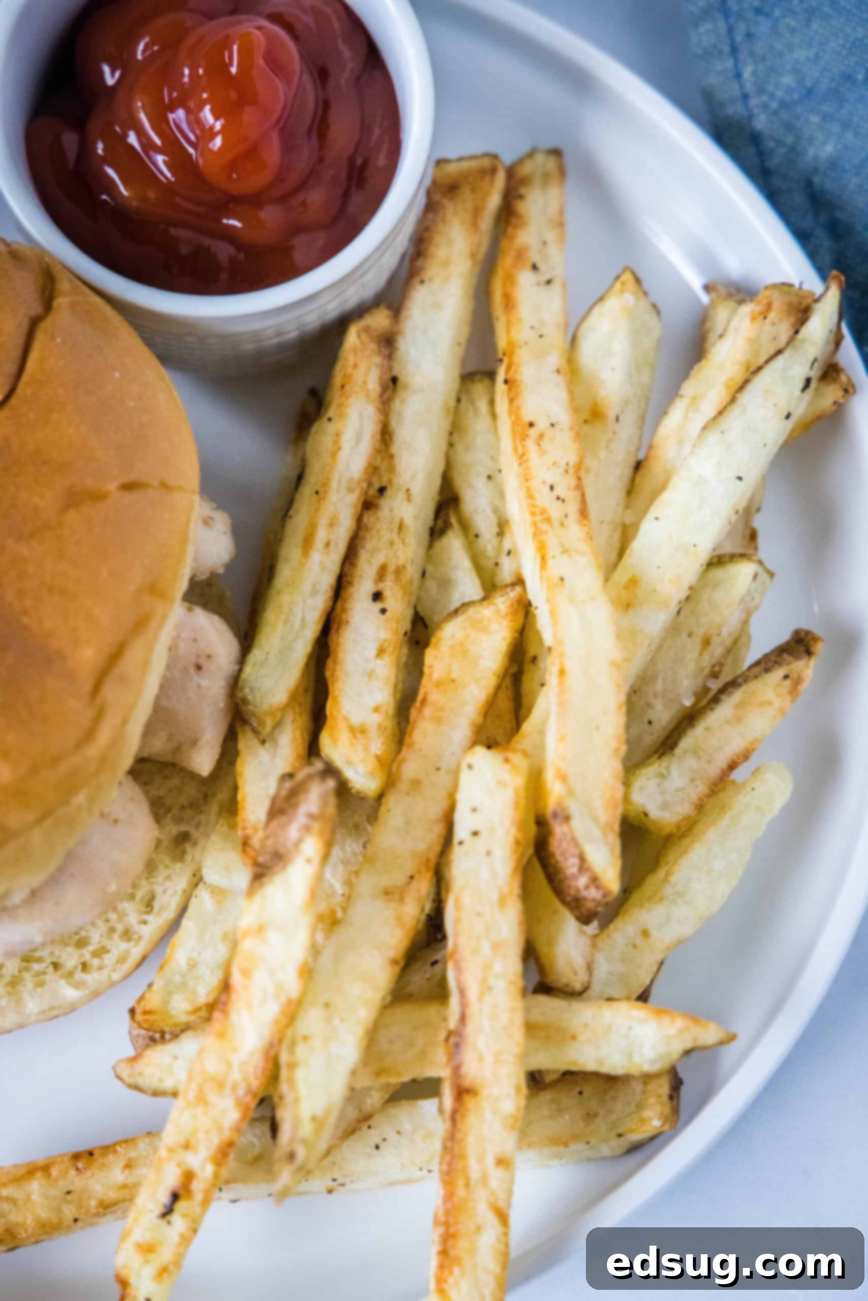 Homemade air fryer French fries are just as crispy as regular fries! Make them in a fraction of the time, with any seasonings you’d like. Overhead view of homemade air fryer French fries next to a burger and a small ramekin filled with ketchup on a plate.