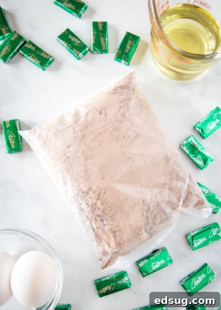 A collection of ingredients for Andes Mint Cookies laid out: a box of Devil's Food cake mix, vegetable oil, eggs, and unwrapped Andes mint candies.