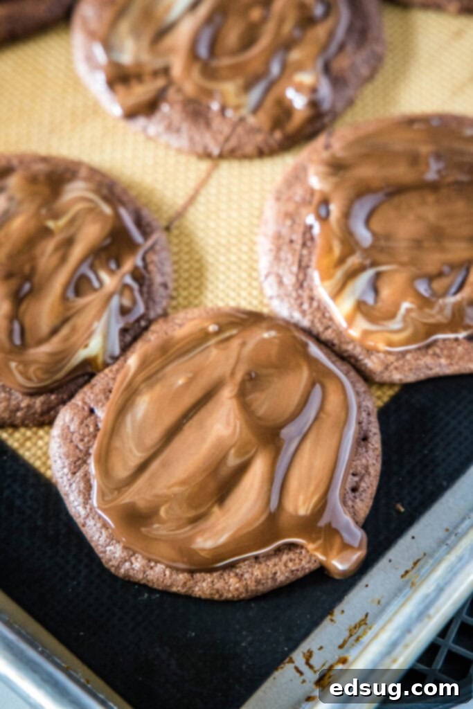 Freshly baked Andes Mint Cookies cooling on a baking sheet, with the melted green mint topping spread over them.