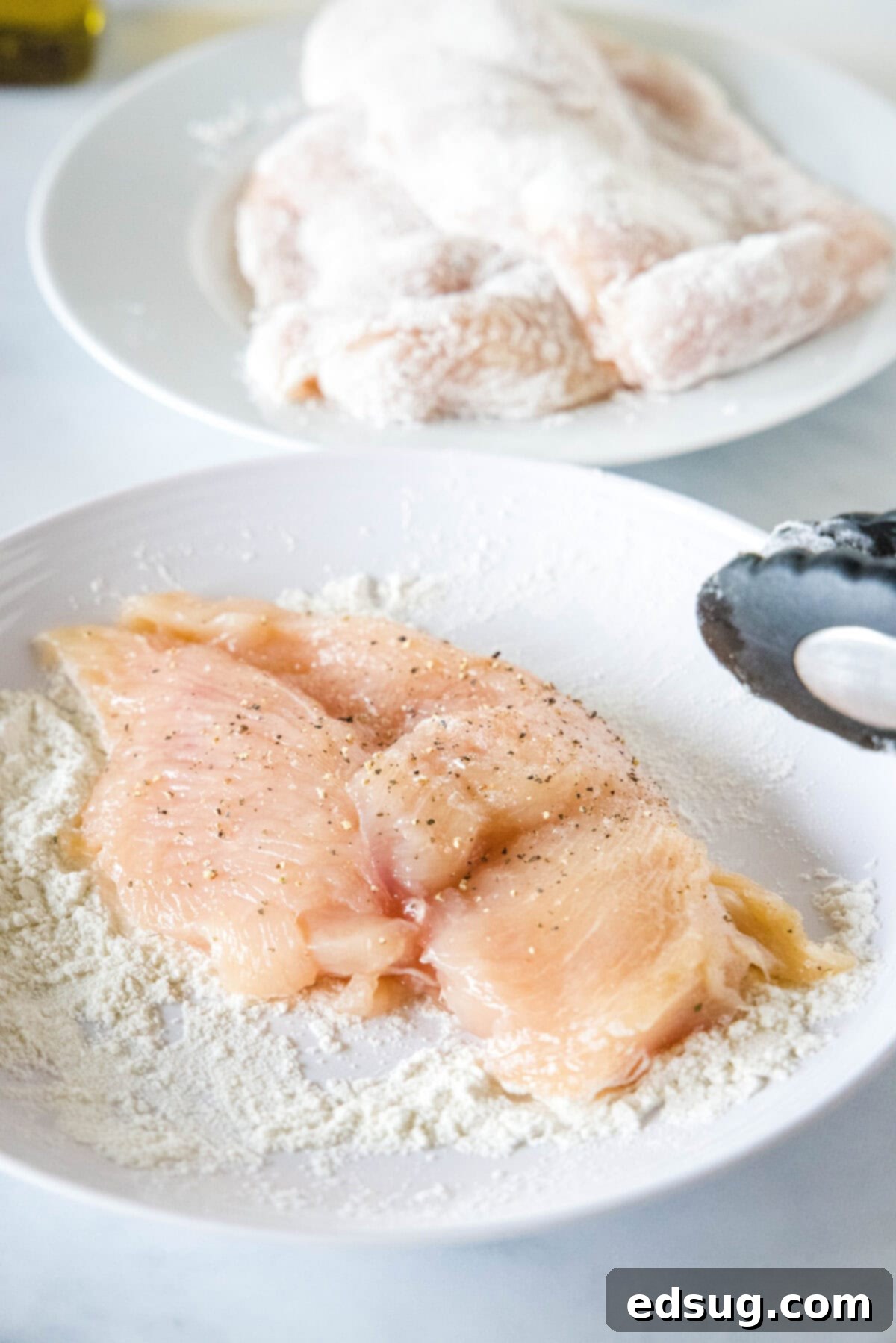Chicken breasts partially dredged in flour inside a shallow bowl.