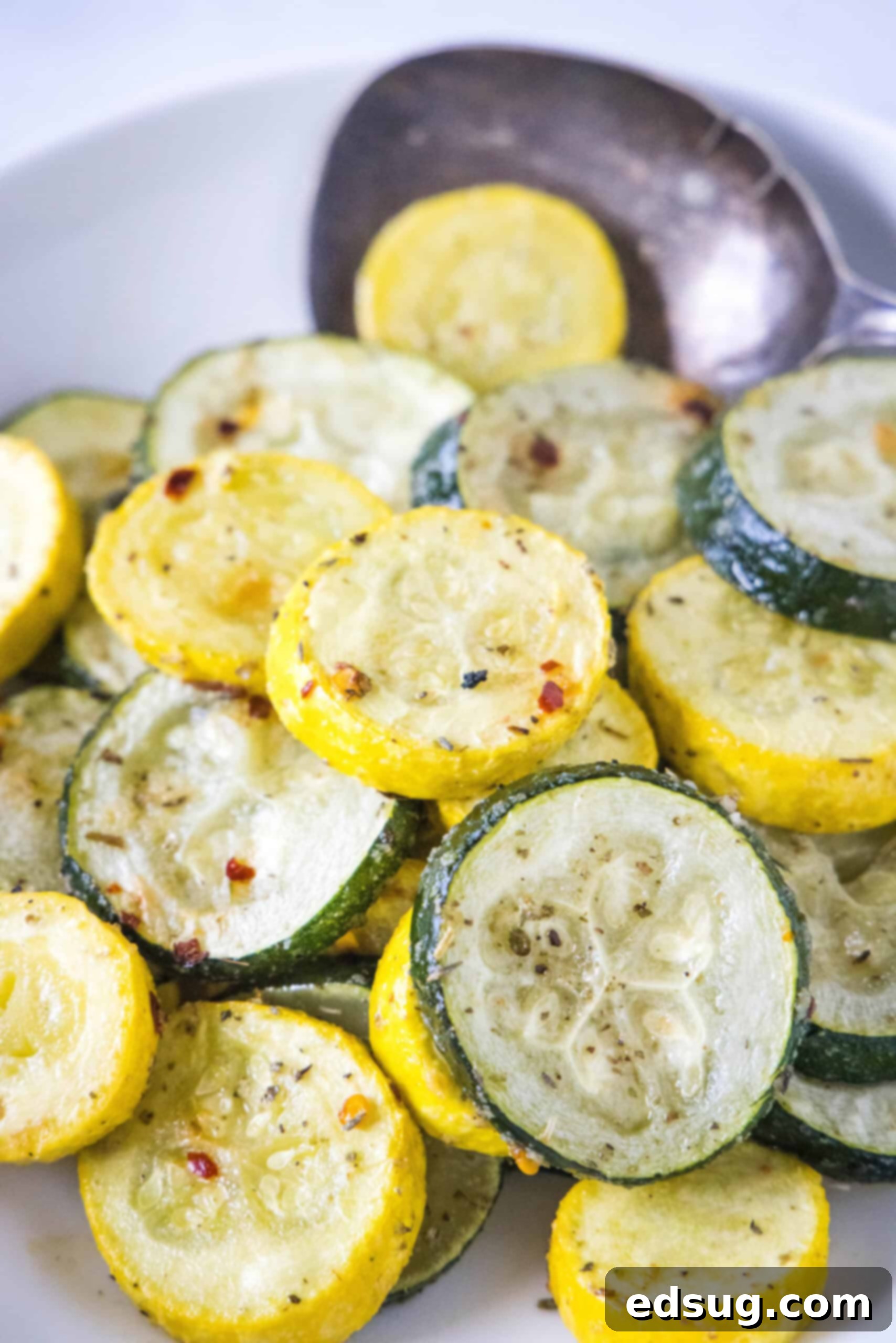 Roasted zucchini and squash in a bowl with a serving spoon.