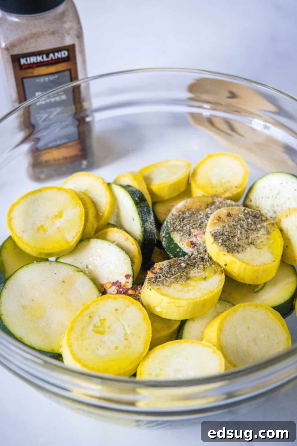 Seasonings added to sliced zucchini and squash in a glass bowll.