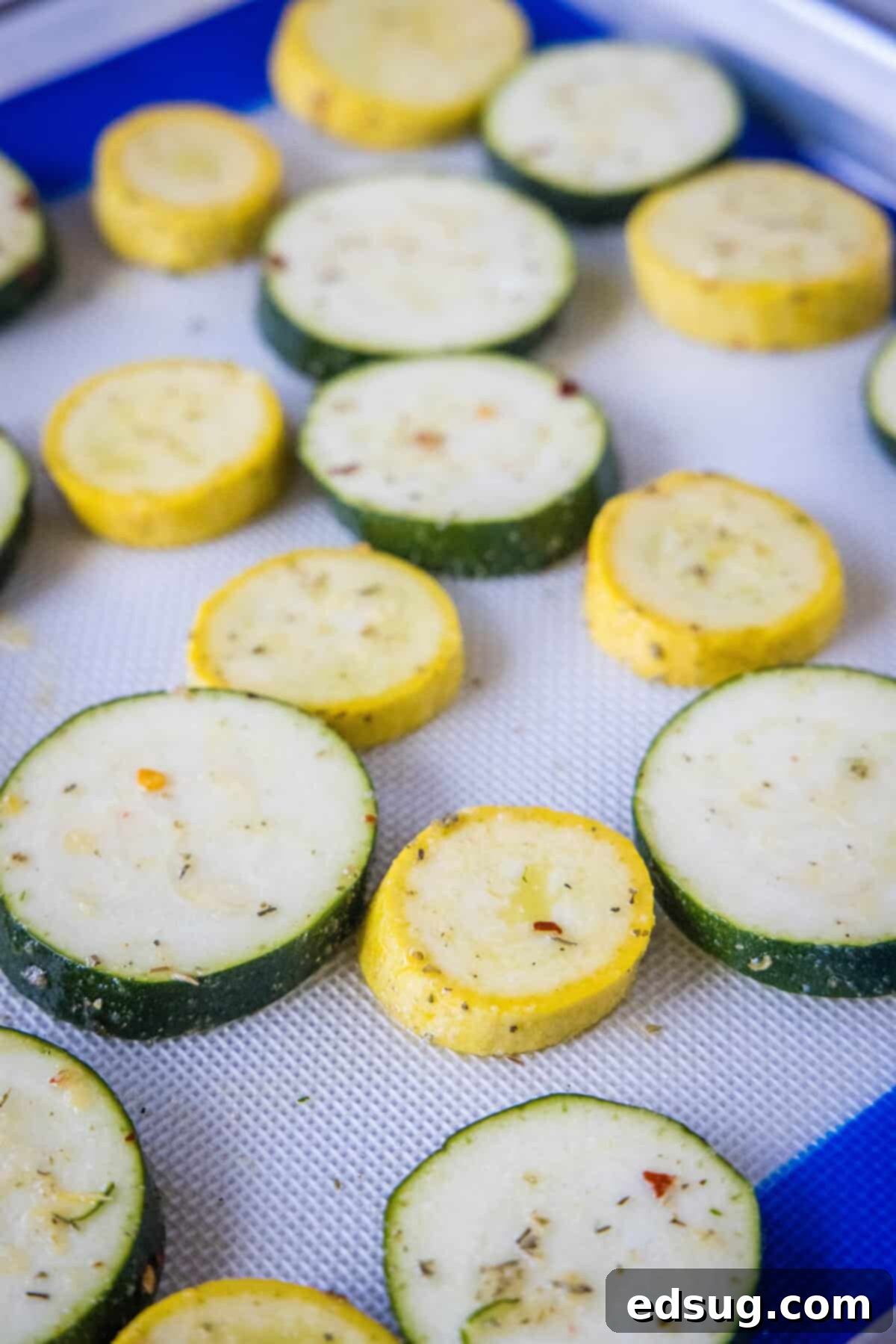 Seasoned squash and zucchini slices arranged in a single layer on a lined baking sheet.