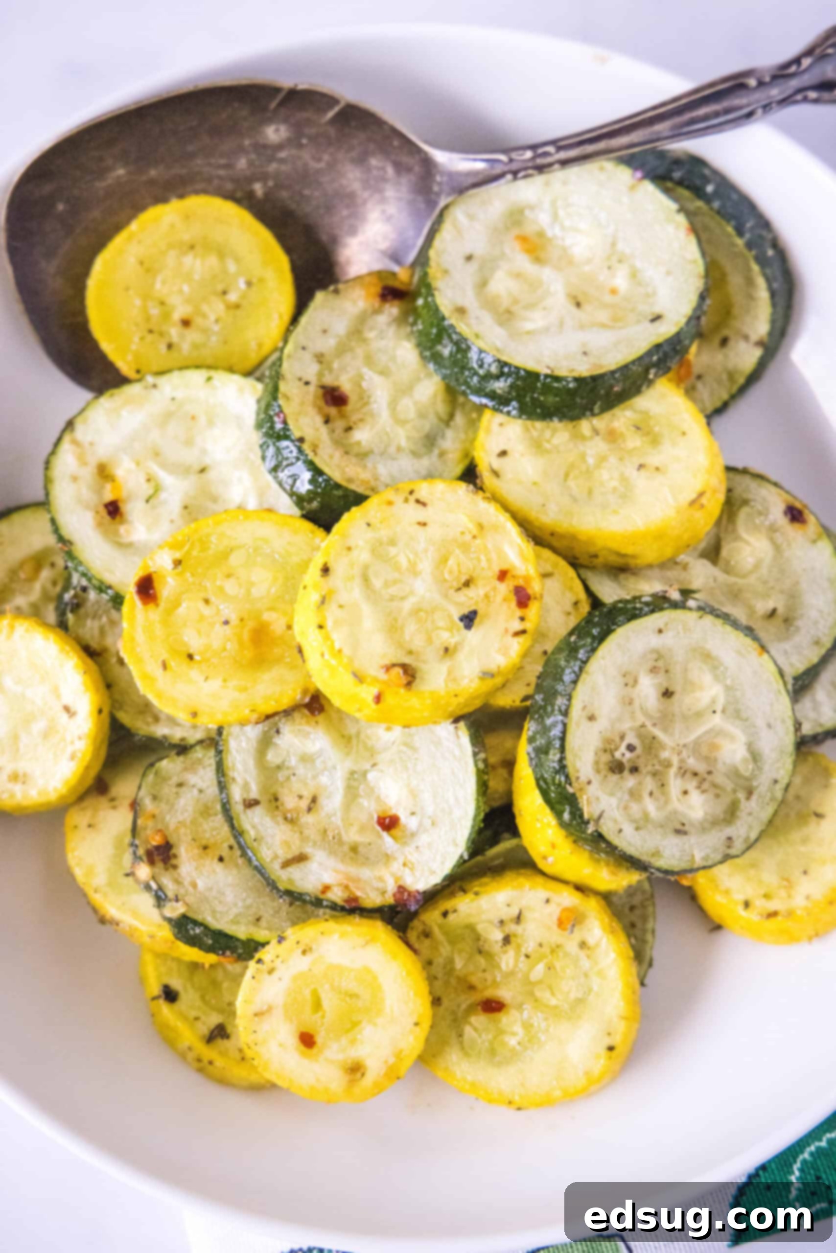 Overhead view of roasted zucchini and squash in a bowl with a serving spoon.