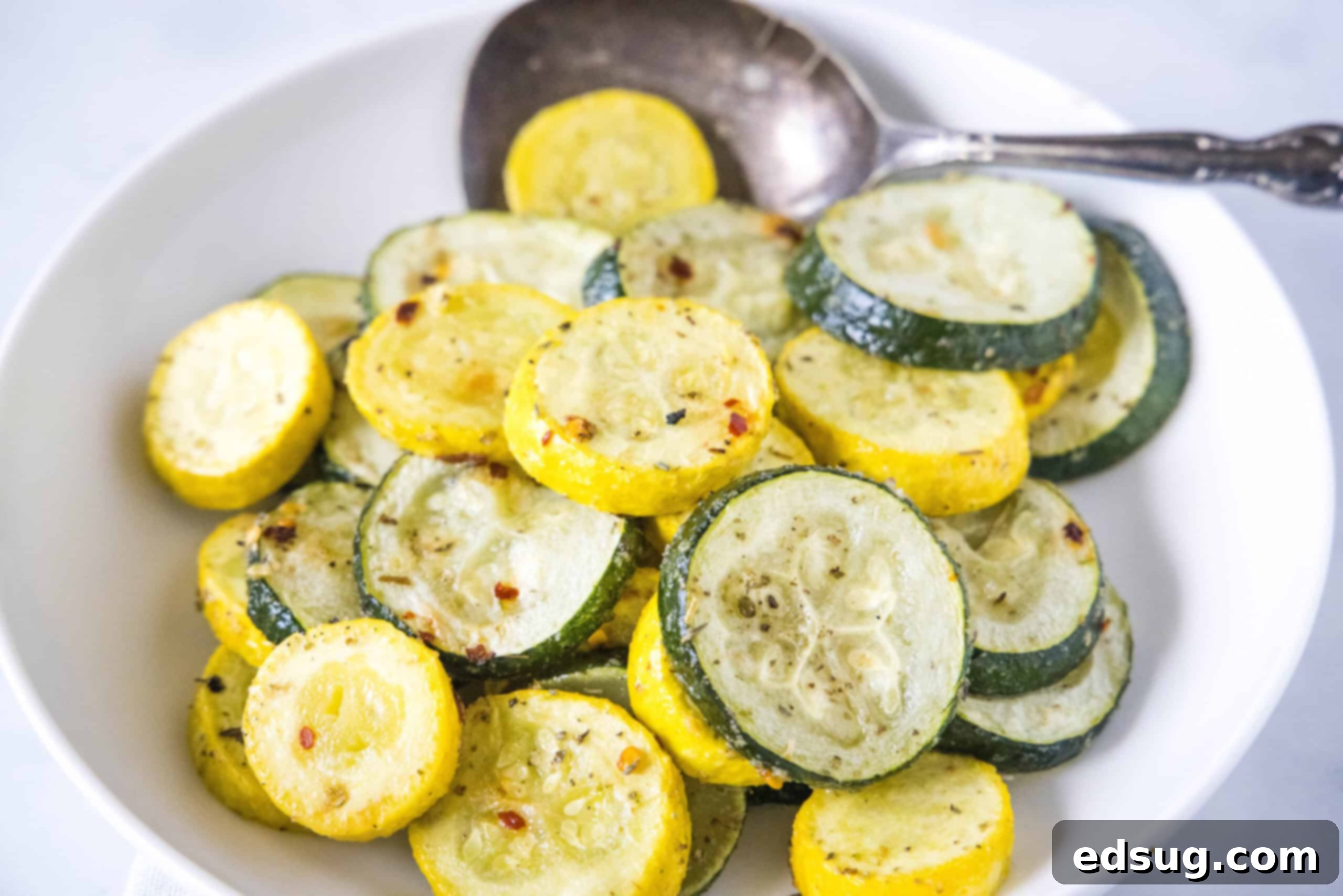 Roasted zucchini and squash in a bowl with a serving spoon.