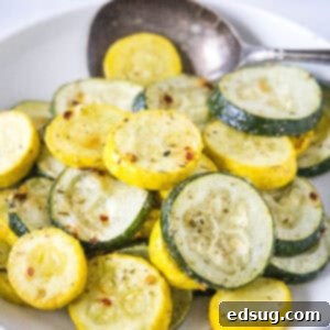 Roasted zucchini and squash in a bowl with a serving spoon.
