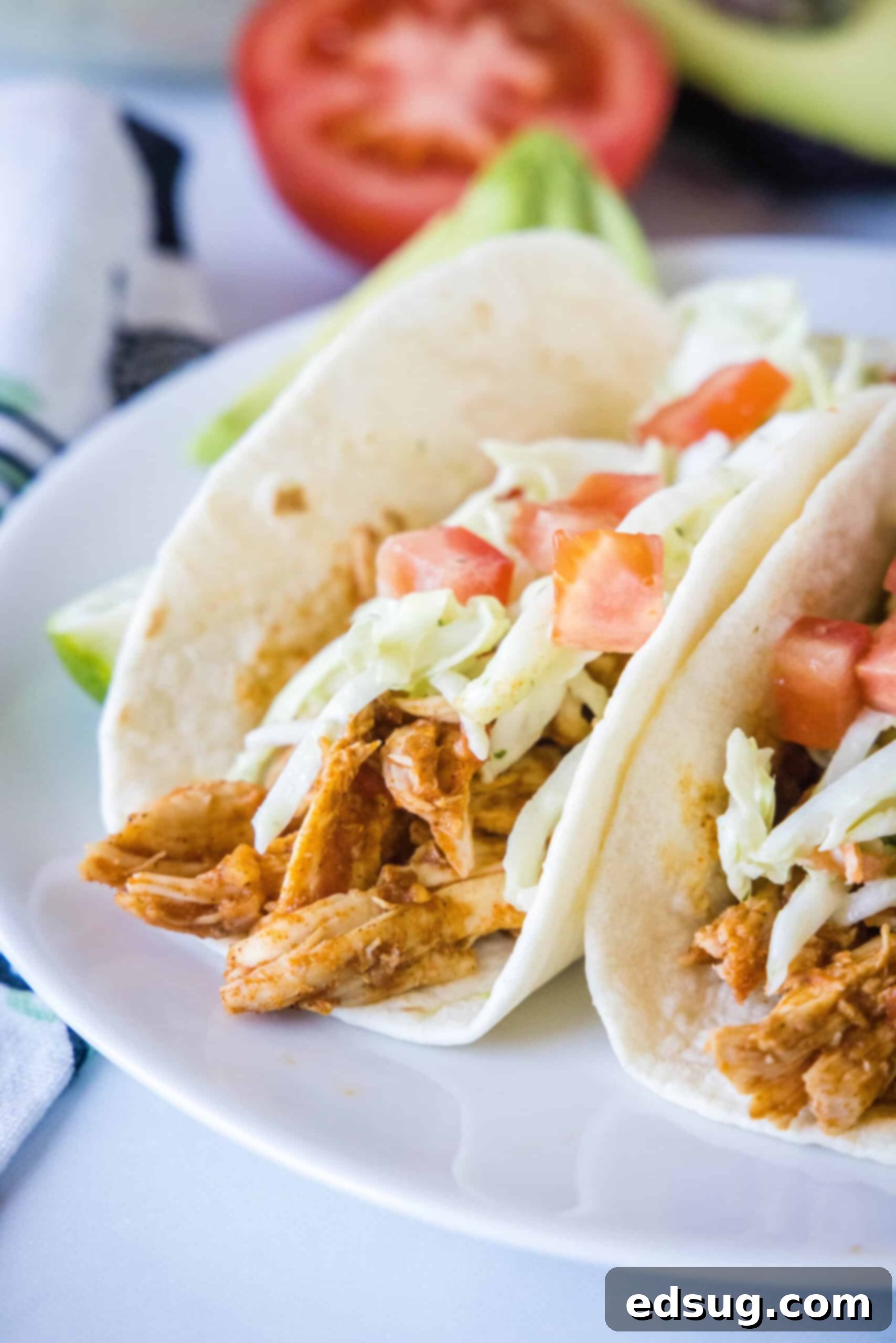 Two rotisserie chicken tacos topped with Mexican coleslaw and diced tomatoes on a white plate.