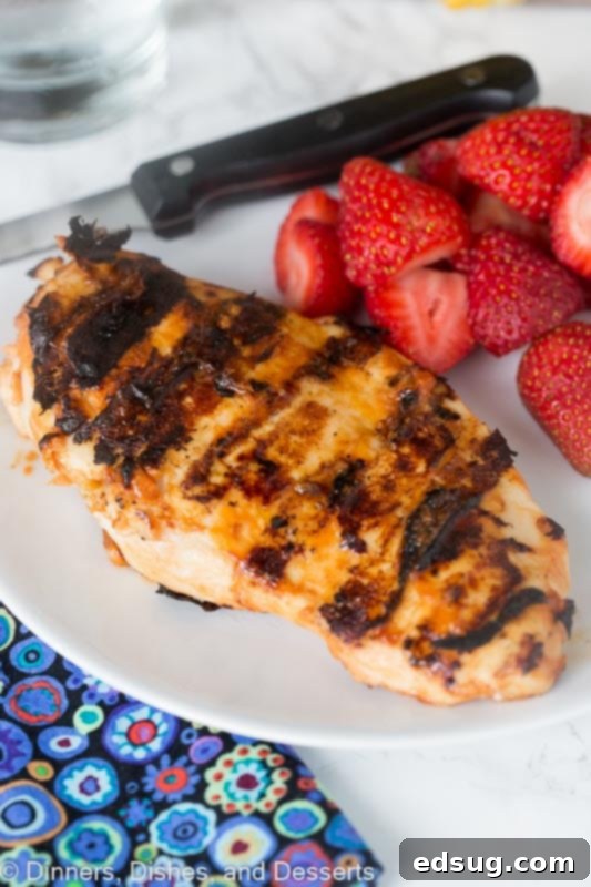 A perfectly grilled chicken breast resting on a plate next to fresh strawberries, showcasing a delicious summer meal.