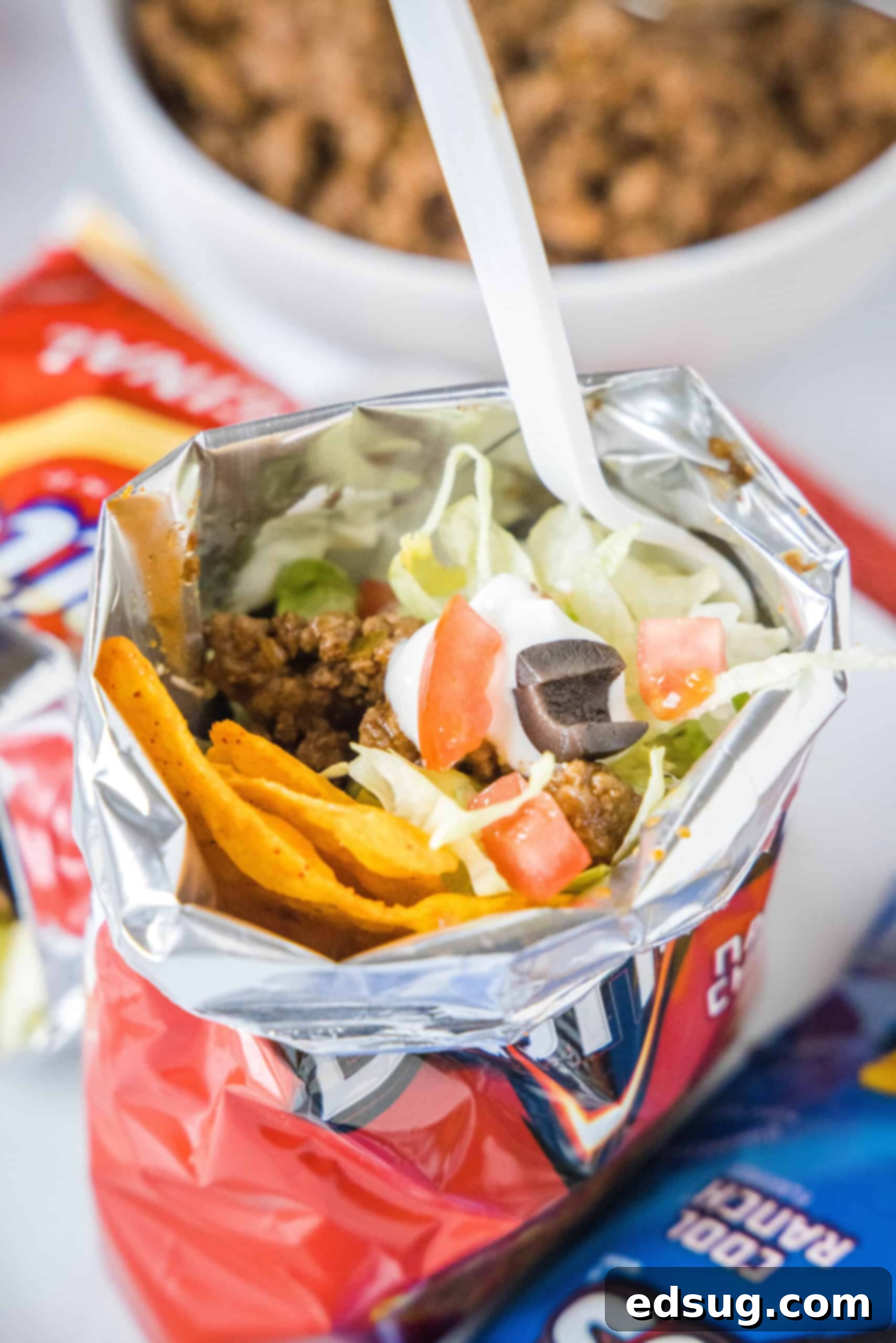The Ultimate Easy Walking Taco Recipe: Fun, Customizable Tacos in a Bag! A walking taco topped with crisp lettuce, fresh tomatoes, and creamy sour cream, served inside a chip bag with a fork ready for enjoyment.