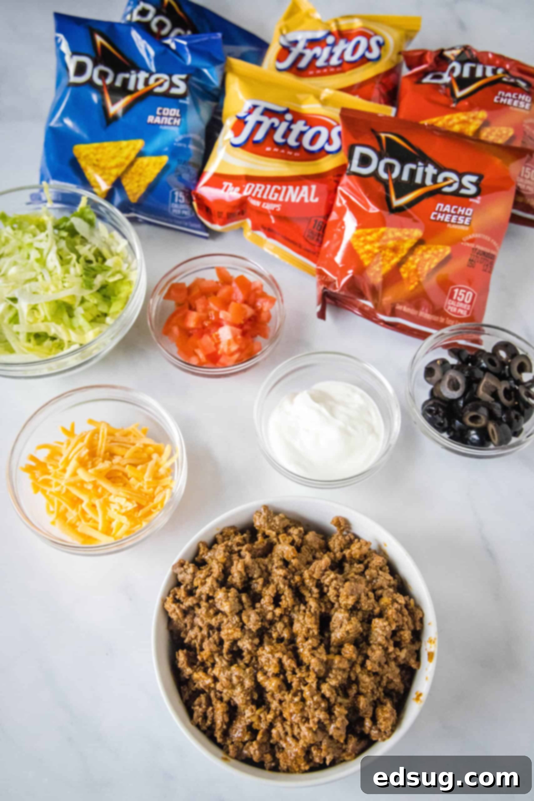 Essential Ingredients for Delicious Walking Tacos An array of fresh ingredients for walking tacos, including ground beef, taco seasoning, various chip bags, and an assortment of colorful toppings.
