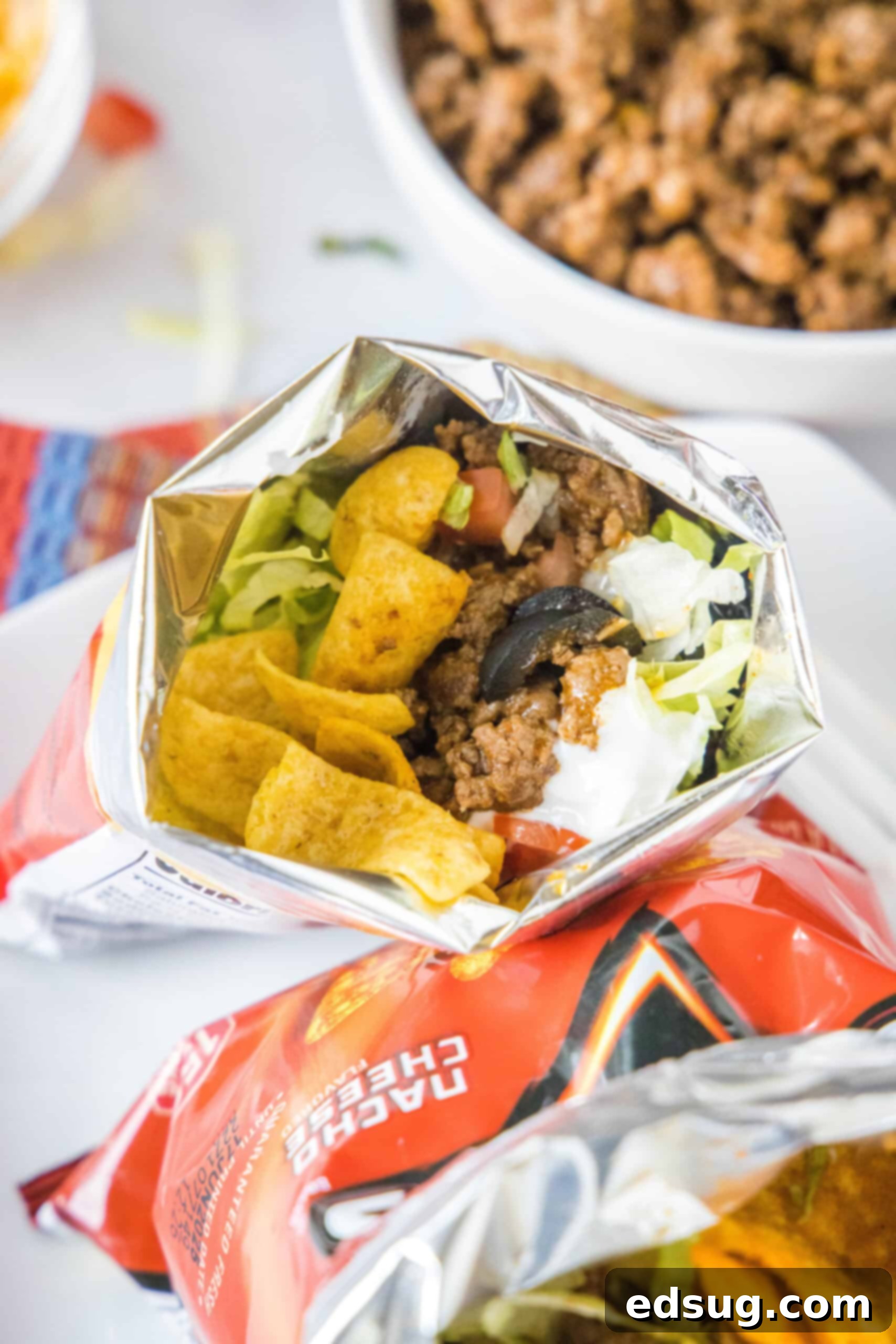 Step-by-Step: Assembling Your Perfect Walking Taco A perfectly assembled walking taco brimming with lettuce, tomatoes, and sour cream inside a chip bag, with a bowl of seasoned taco meat waiting in the background.