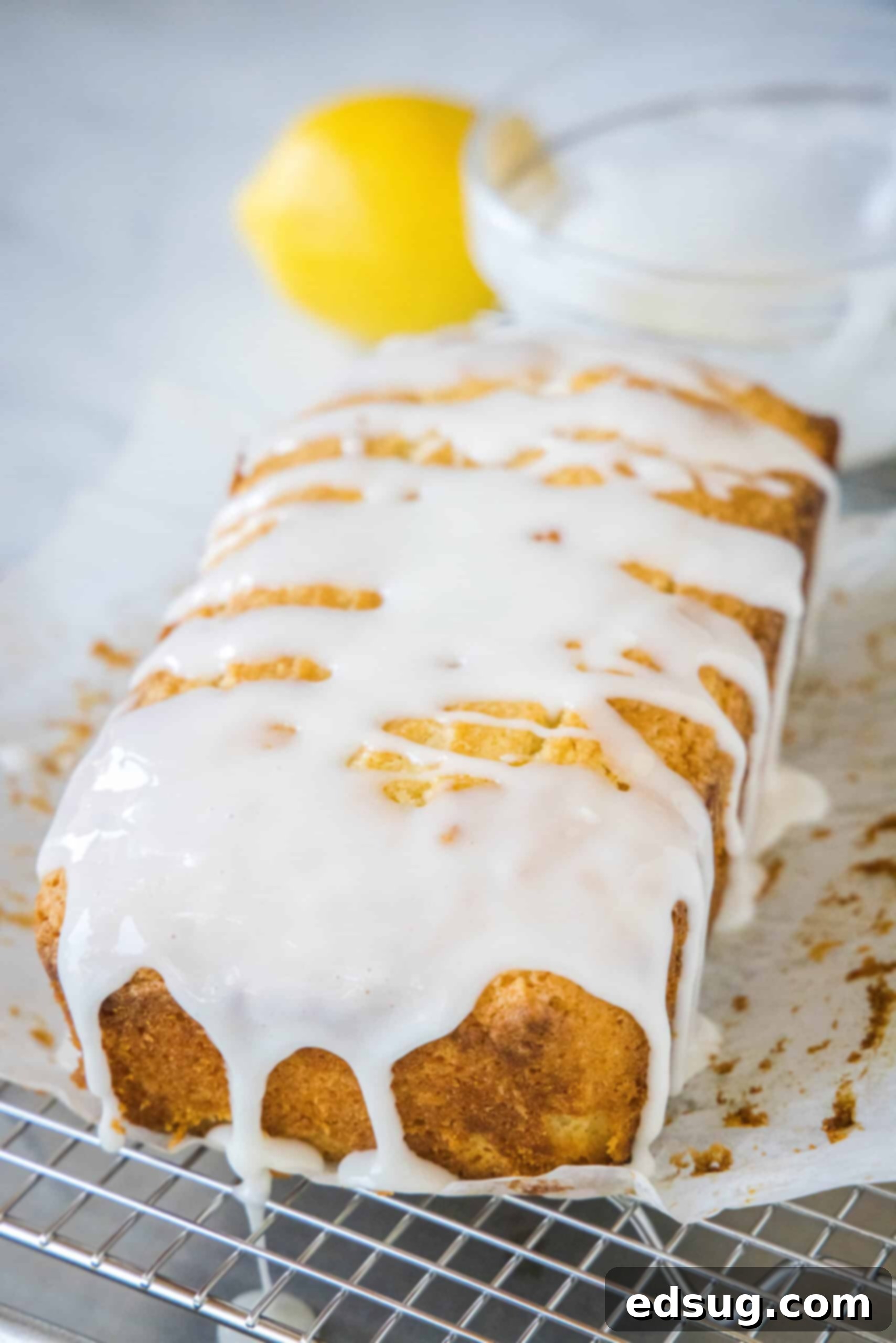 A beautifully glazed lemon loaf resting on parchment paper over a wire cooling rack, ready to be sliced.