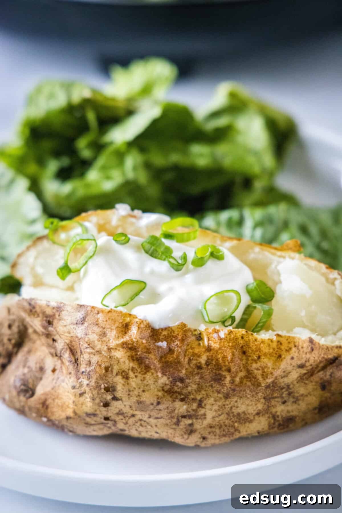 A perfectly cooked baked potato on a plate, generously topped with creamy sour cream and fresh chives, ready to be enjoyed.