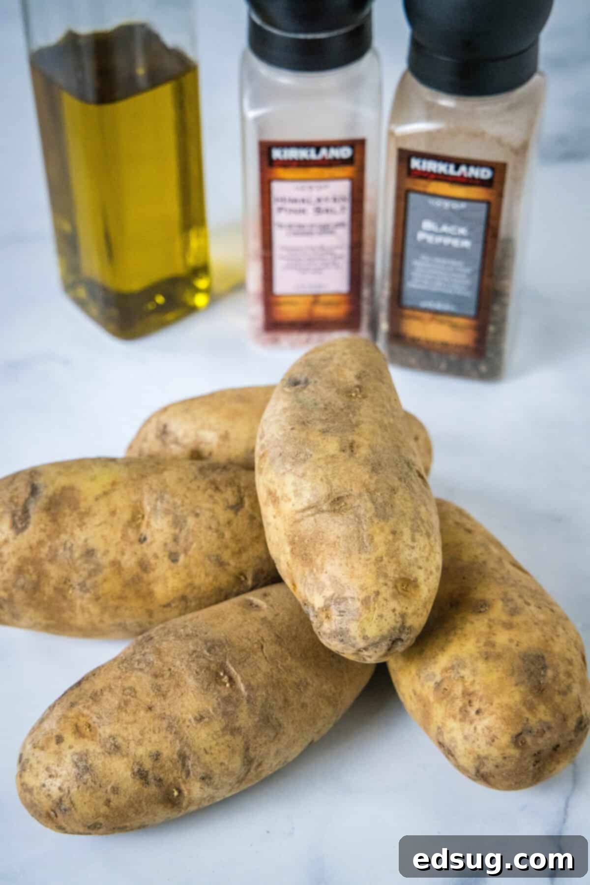 Essential ingredients for slow cooker baked potatoes: fresh russet potatoes, a bottle of olive oil, and shakers of salt and pepper, laid out on a clean surface.