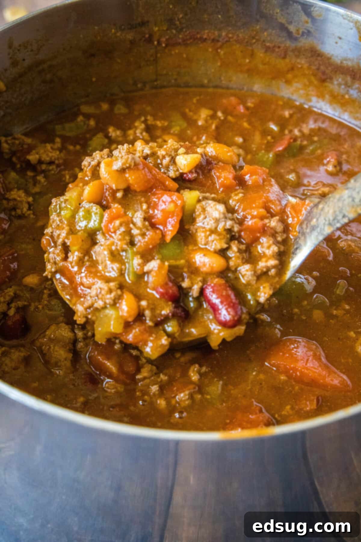 Copycat Wendy's Chili Recipe 4 A large serving spoon scooping out thick, hearty chili from a simmering pot, showcasing its rich texture and plentiful ingredients.