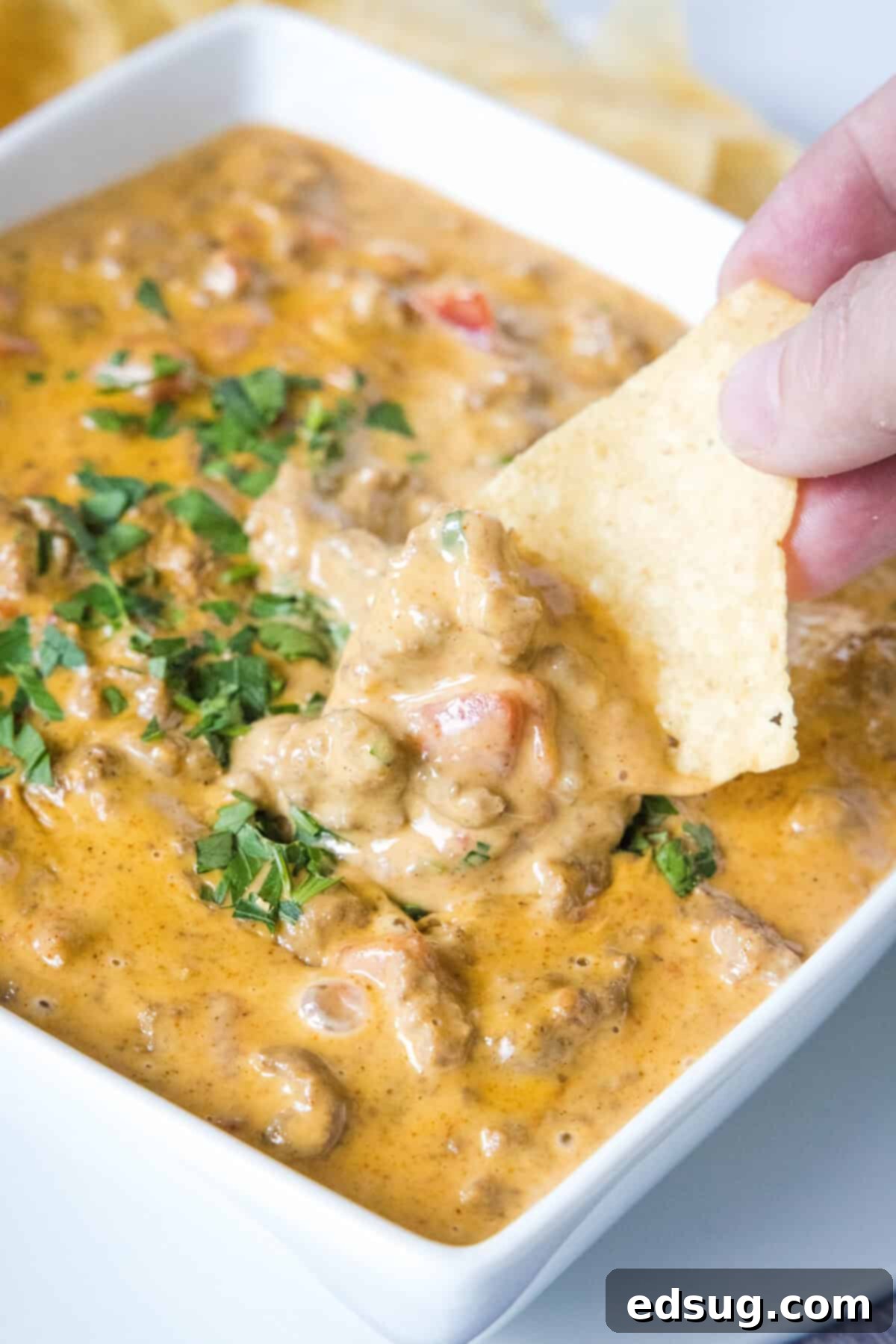 The Go-To Rotel Cheese Dip 2 scooping cheesy rotel dip out of bowl with a tortilla chip