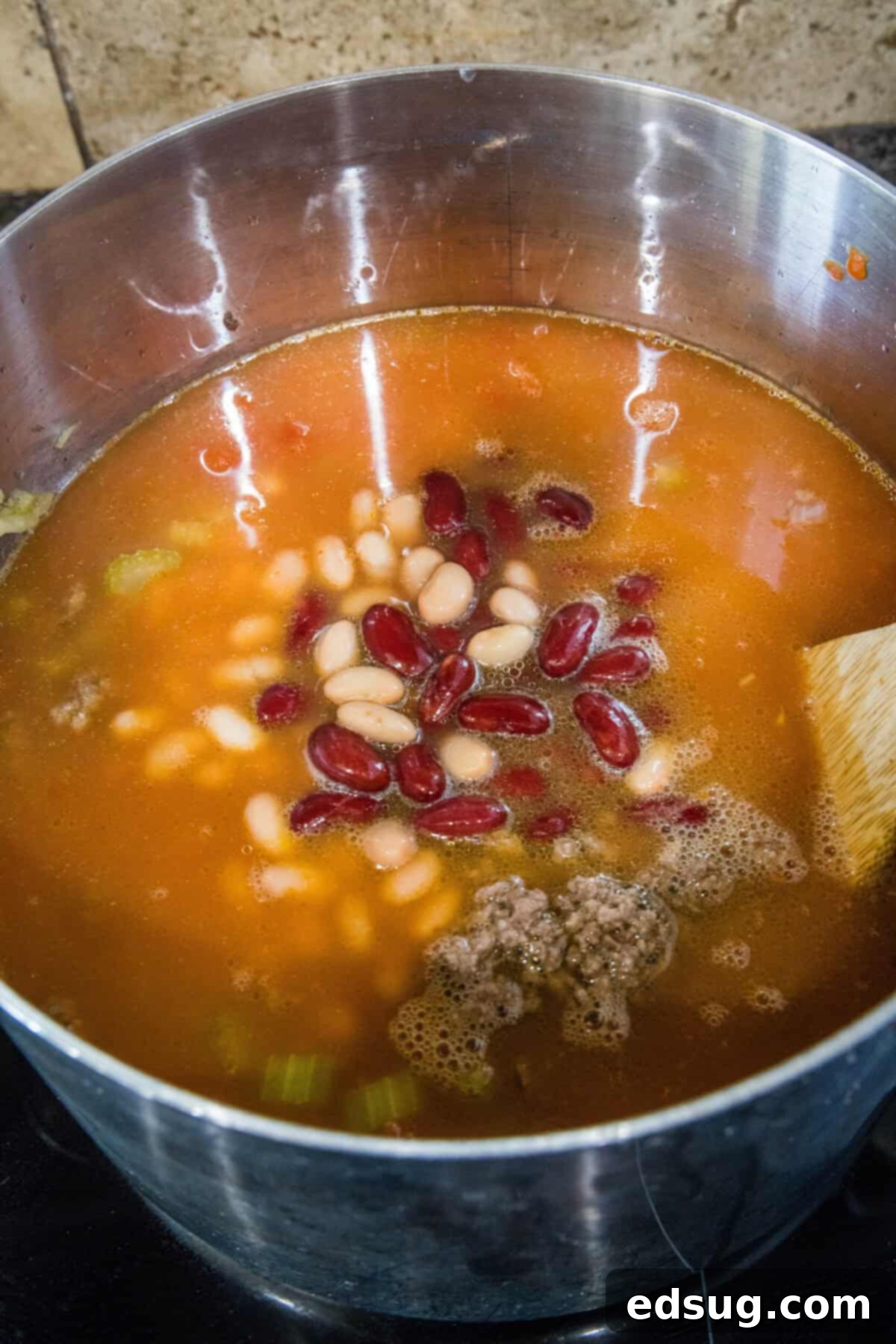 Pasta and Beans 5 Various soup ingredients, including canned tomatoes and beans, being added to the sautéed vegetables in a large pot, ready for simmering.