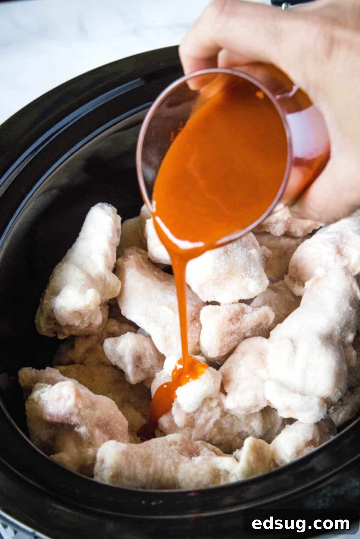 Fall-Off-The-Bone Crockpot Wings 3 pouring buffalo sauce over chicken wings in a crockpot