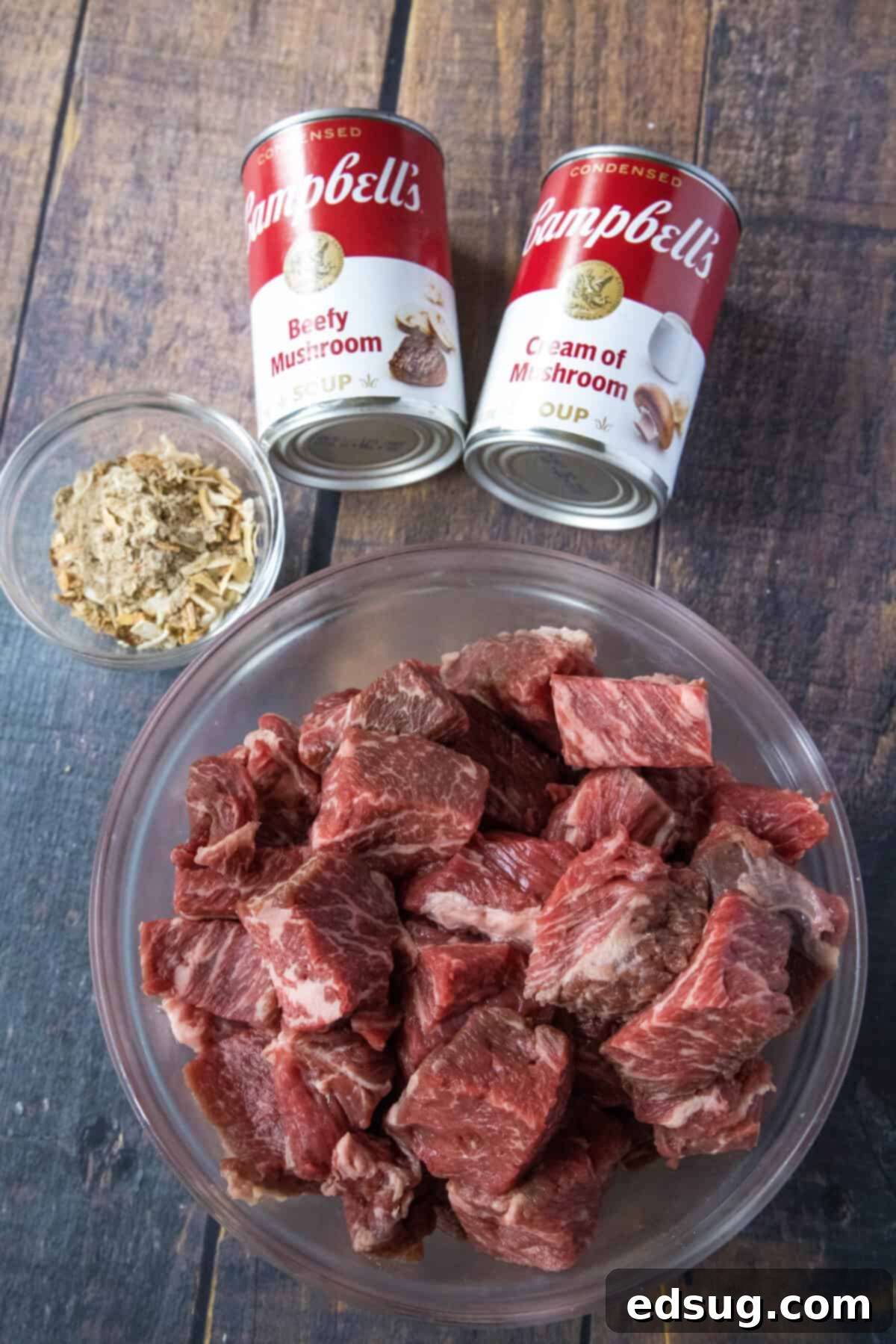 Simple ingredients laid out for making No Peek Beef Tips, including stew meat, condensed soups, and onion soup mix.