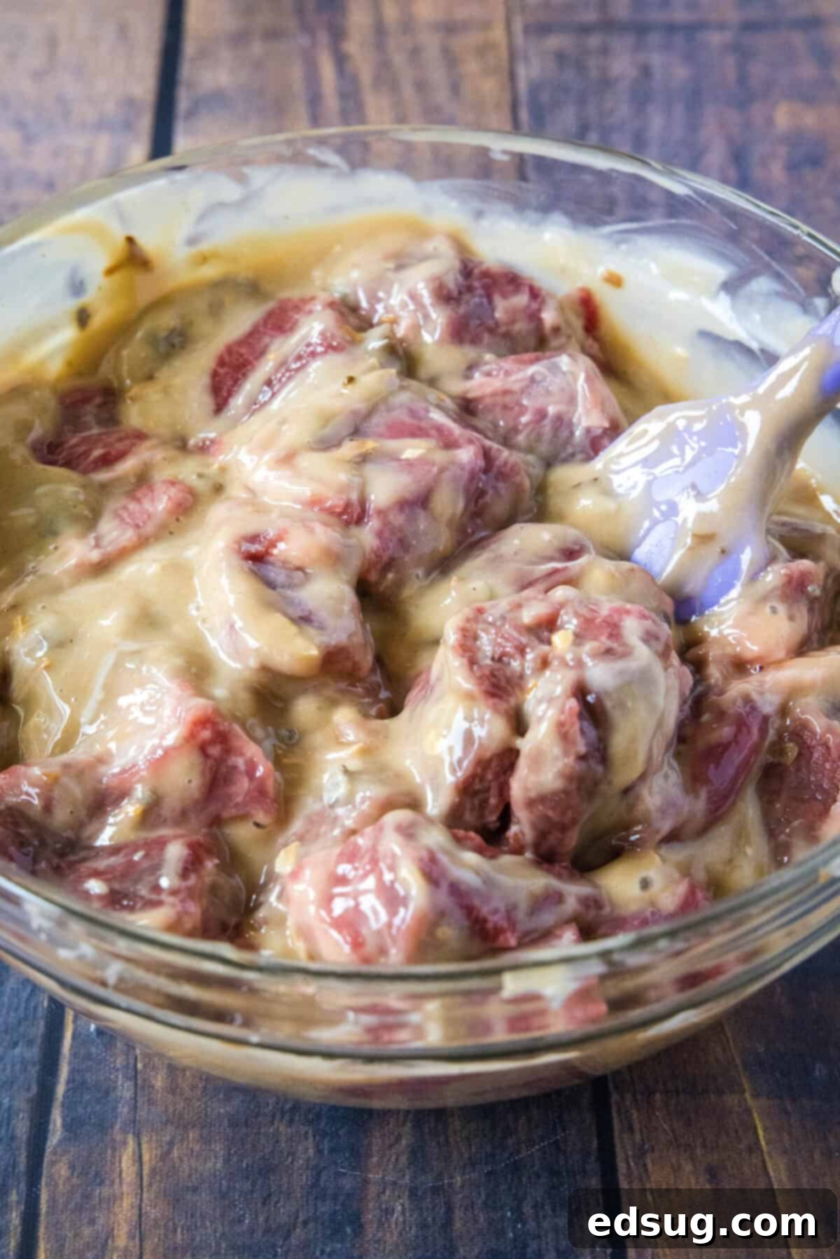 Cubed beef tips being coated thoroughly in the creamy soup and onion soup mix mixture in a large mixing bowl.