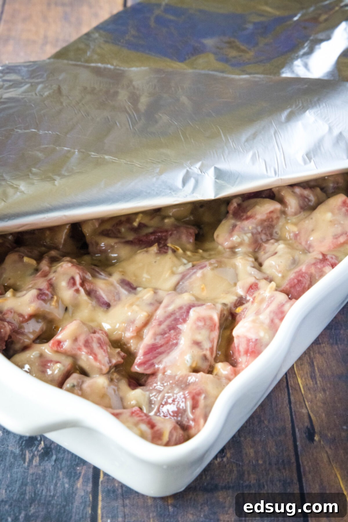 Casserole dish filled with coated beef tips, tightly covered with foil and ready to be placed in the oven.