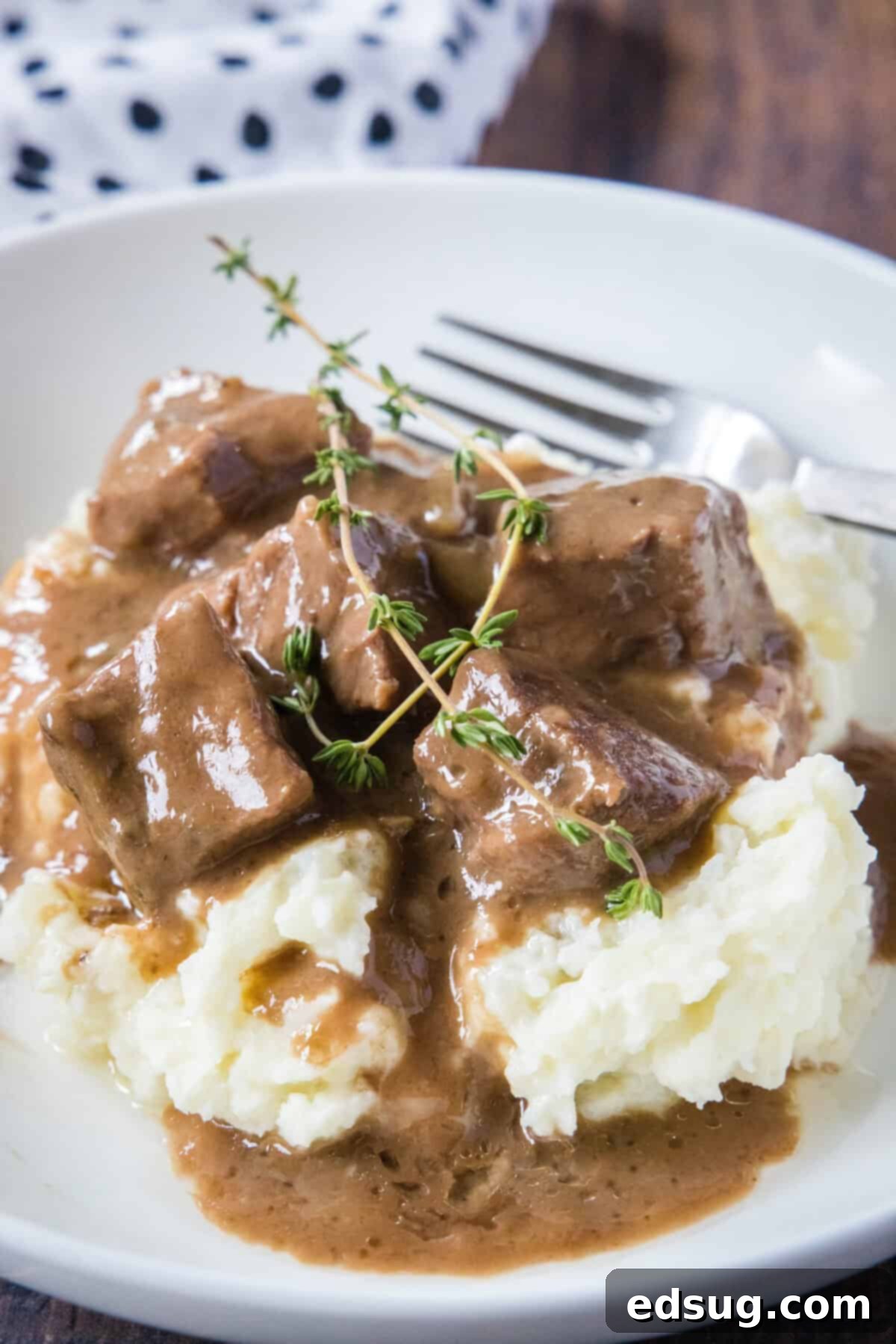 A white bowl showcasing a generous serving of No Peek Beef Tips and gravy over mashed potatoes, garnished with fresh parsley.