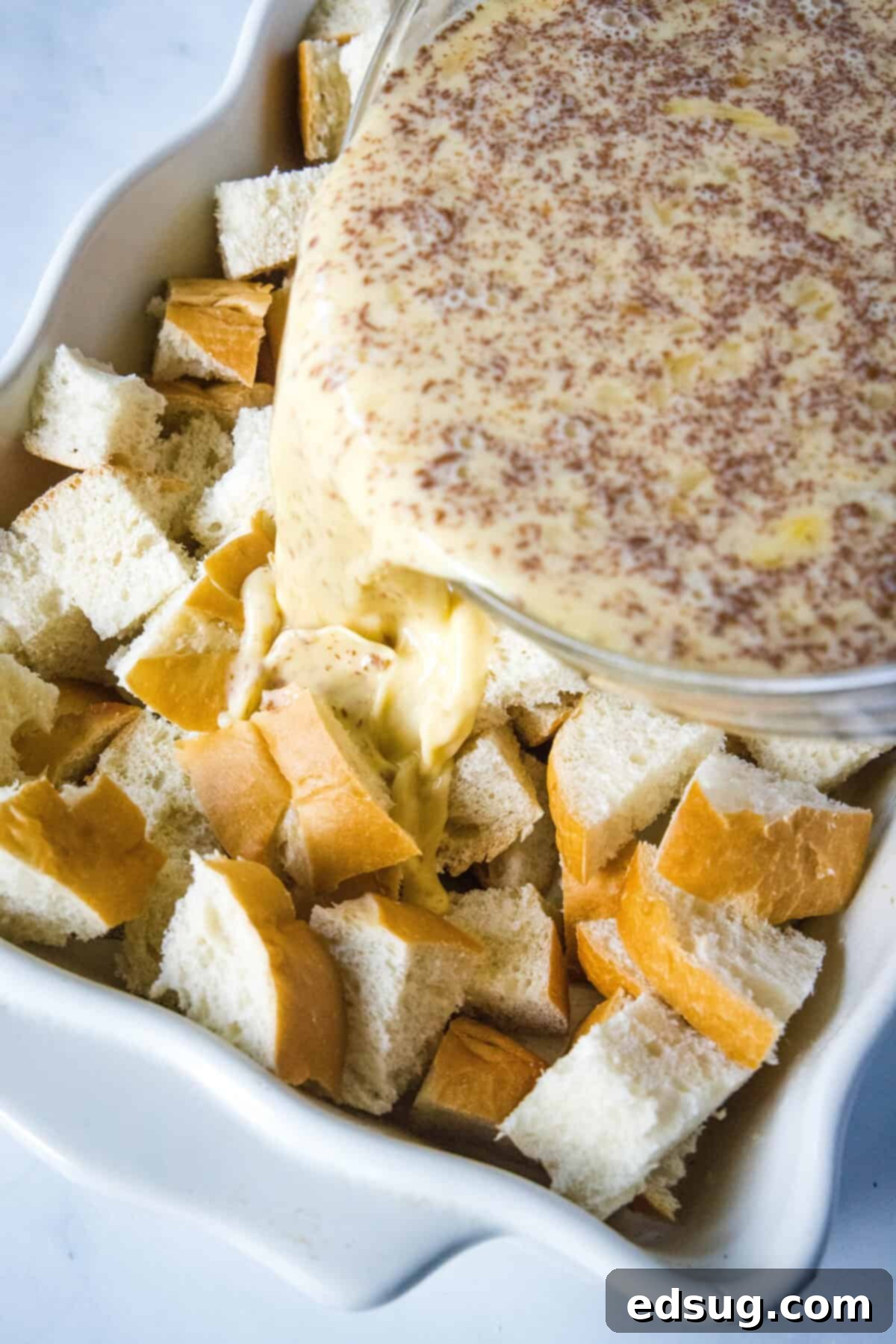 Sleep-In French Toast Casserole 4 pouring egg custard over bread cubes in a baking dish
