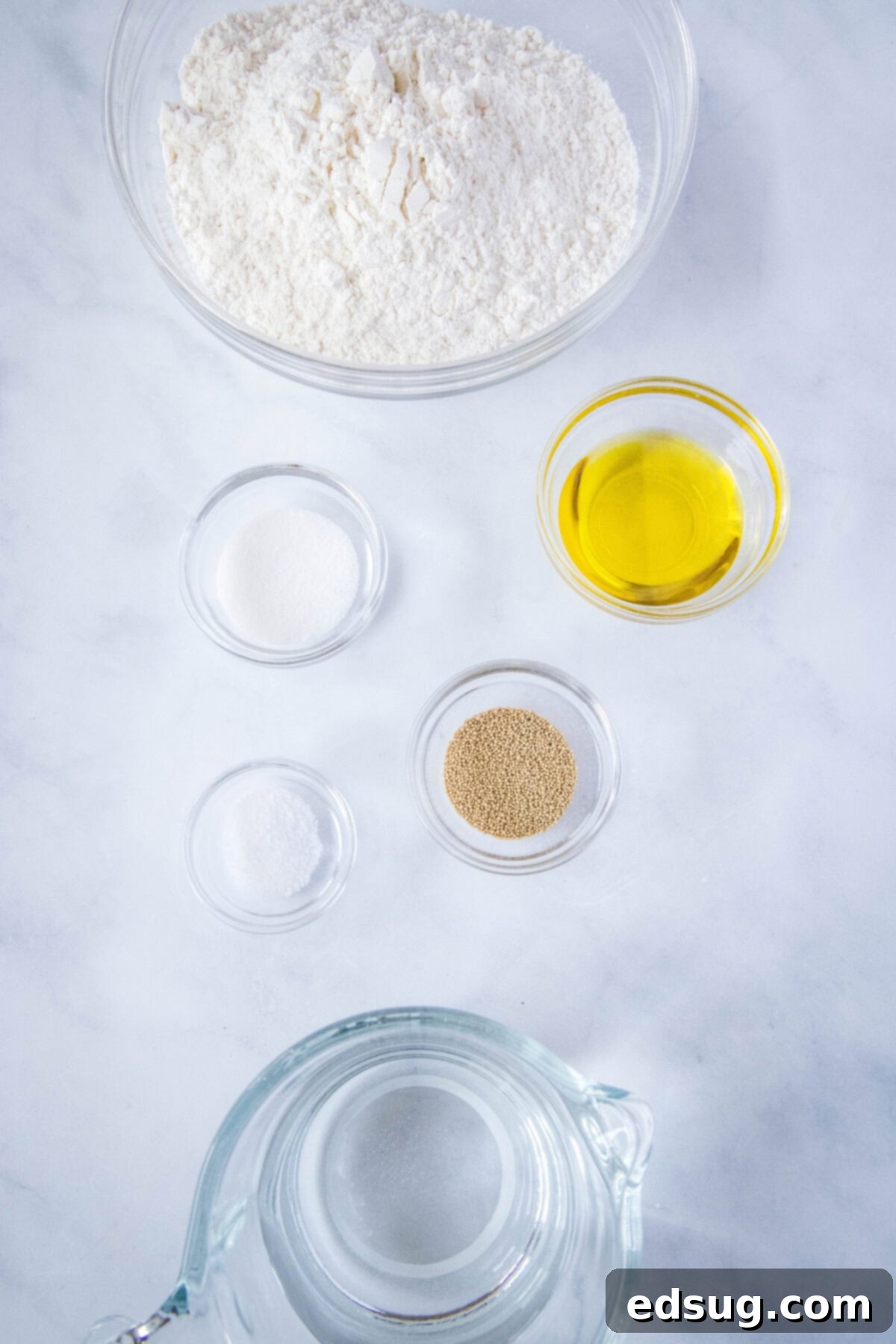 Effortless Slow Cooker Bread 3 A collection of ingredients for slow cooker bread, including flour, yeast, sugar, salt, olive oil, and warm water, arranged neatly on a counter.