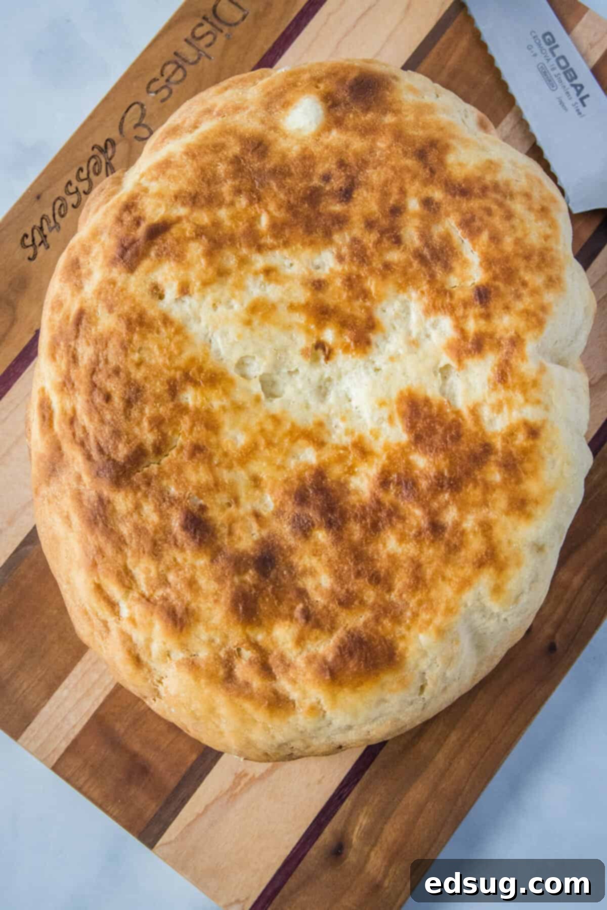 Effortless Slow Cooker Bread 8 A whole loaf of freshly baked slow cooker bread, golden-brown on top, resting on a wooden cutting board with a knife, ready for slicing.