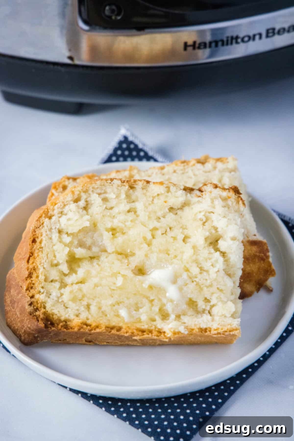 Effortless Slow Cooker Bread 9 Two slices of slow cooker bread, one buttered, on a small white plate next to a stick of butter and a knife, ready to eat.
