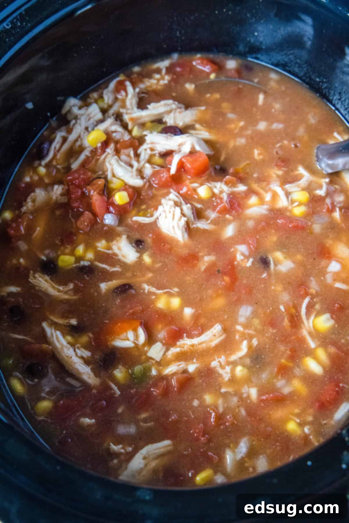Cooked chicken tortilla soup simmering in a crockpot, ready for shredding the chicken.