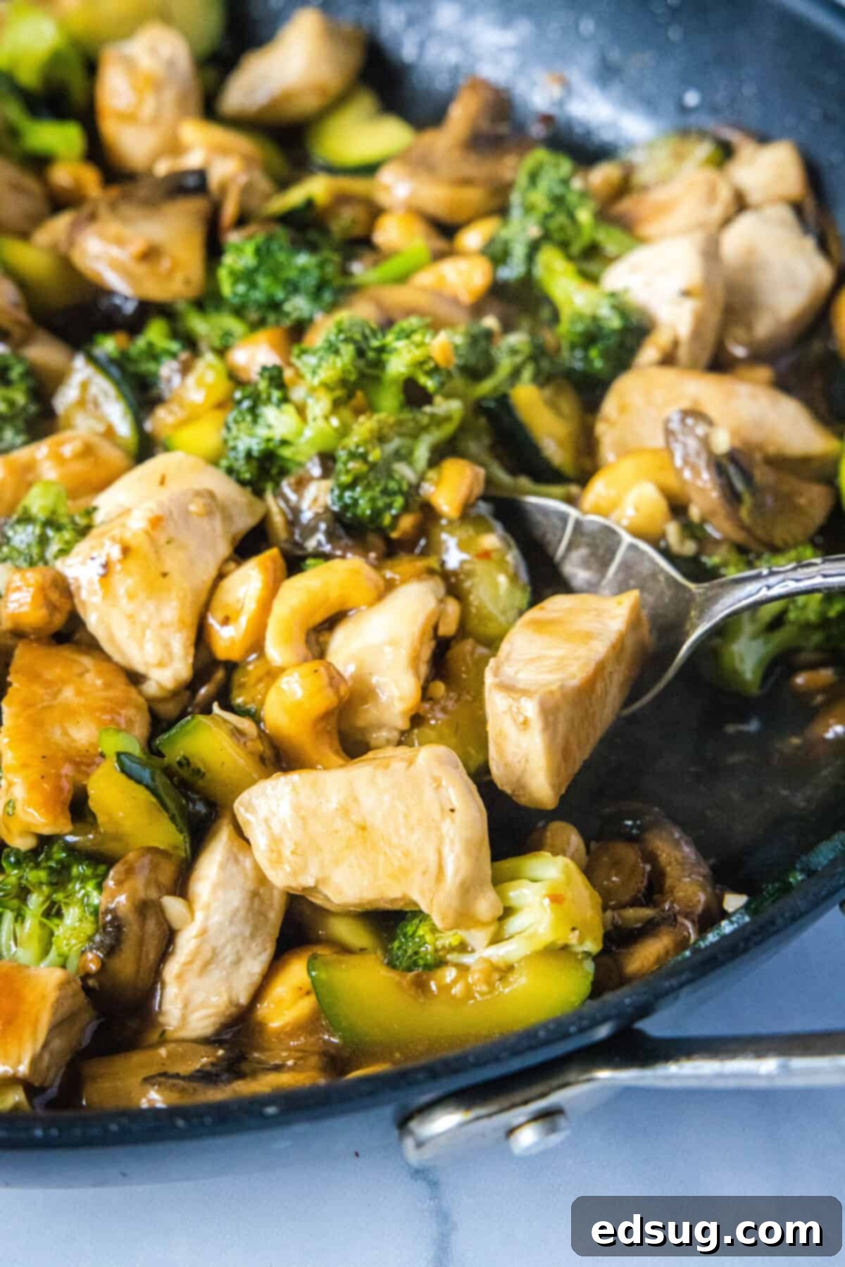 scooping chicken stir fry from skillet, a close up shot showing tender chicken and vibrant vegetables coated in a glossy sauce